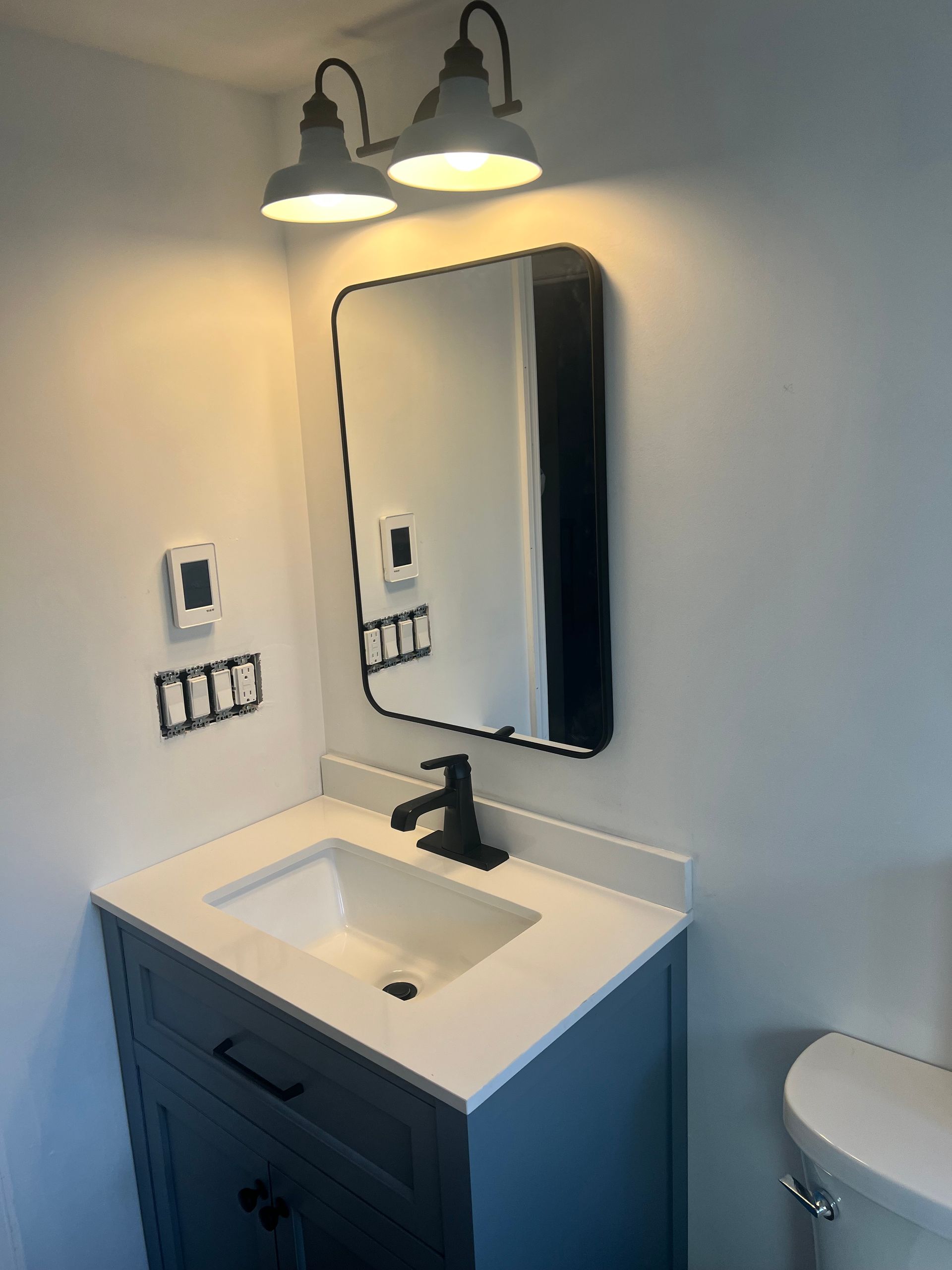 Bathroom with blue vanity, white countertop, black faucet, mirror, and two-bulb light fixture.