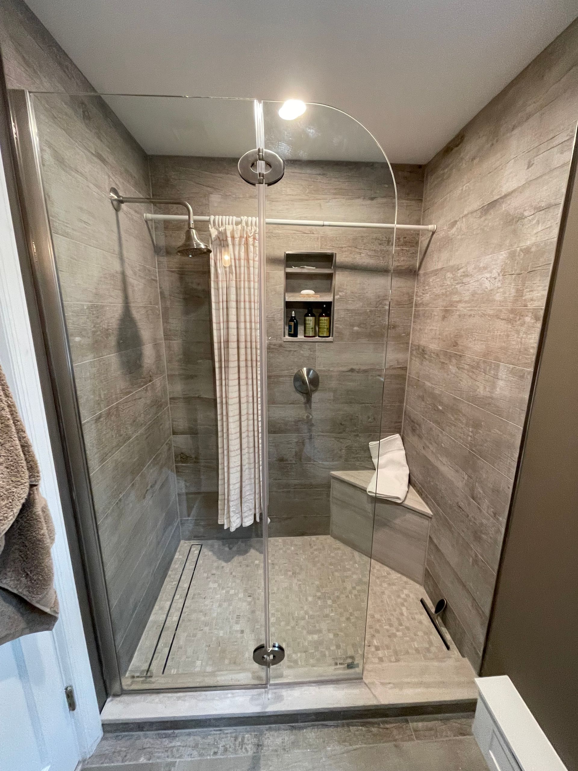 Modern shower with glass door and stone tile walls. Includes a built-in bench and recessed shelf.