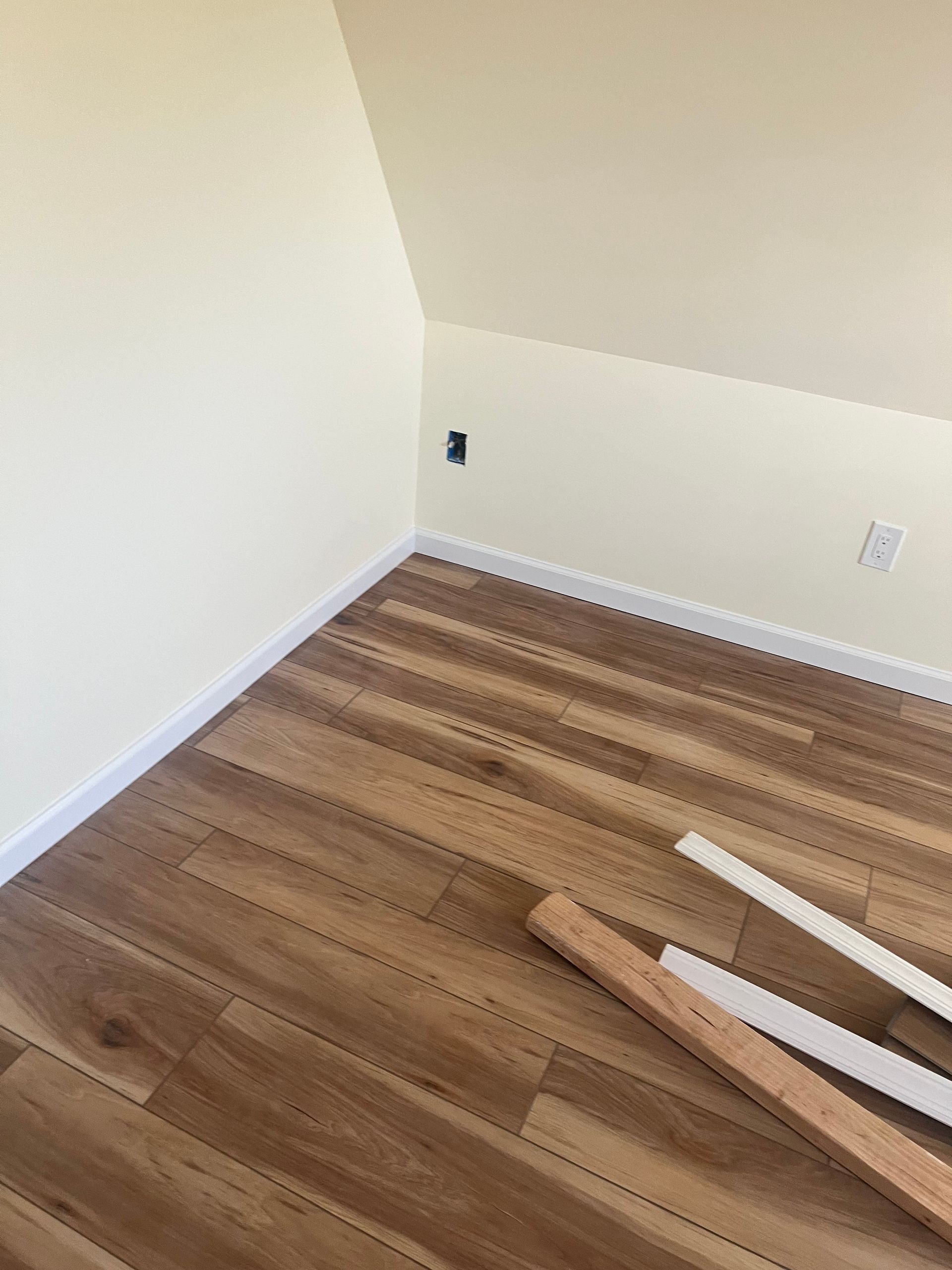 Interior room with wood-look floor, white trim, and angled ceiling. Electrical outlets visible. Light-colored walls.