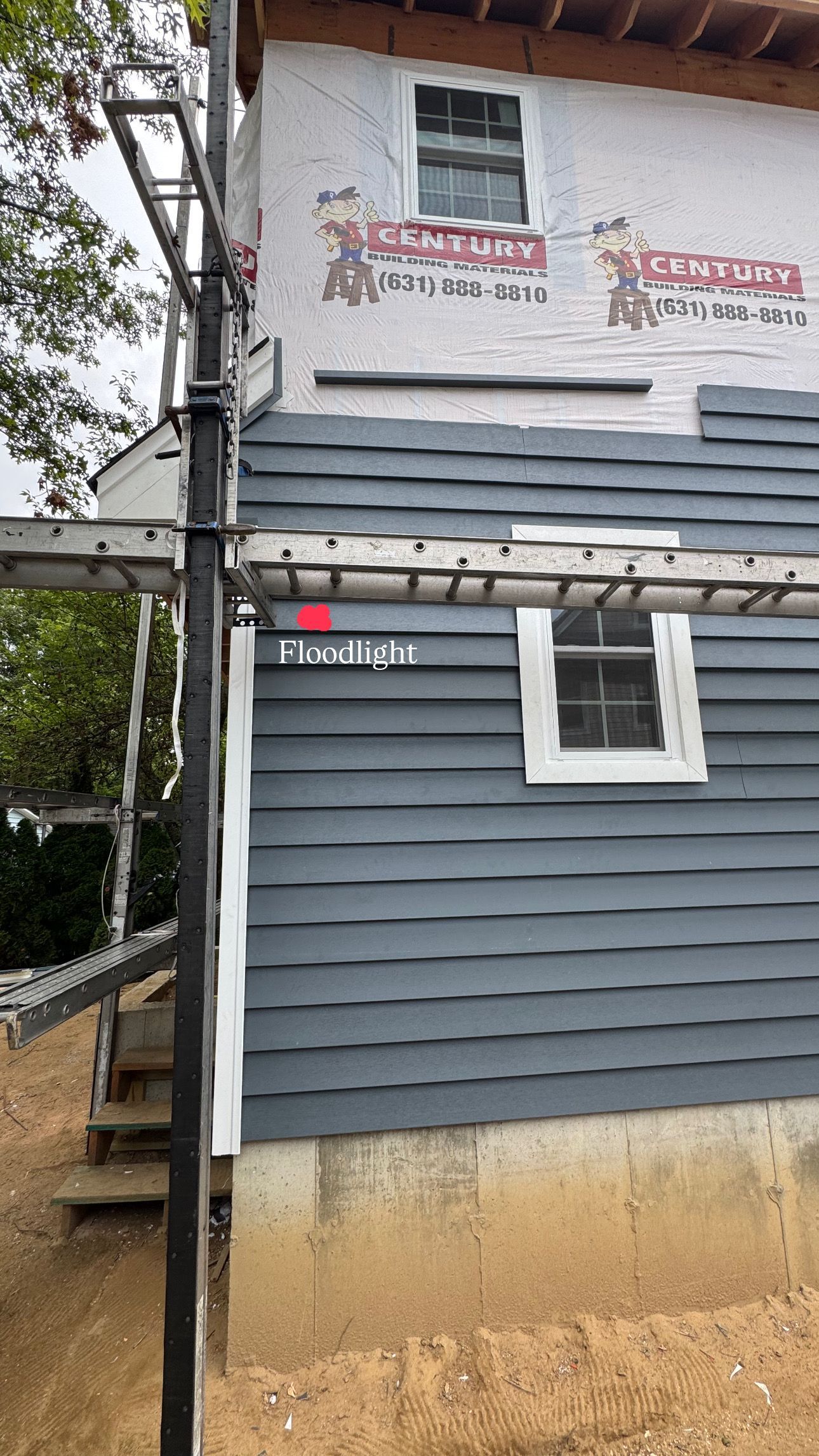Scaffolding next to a house with gray siding under construction and two white-framed windows.