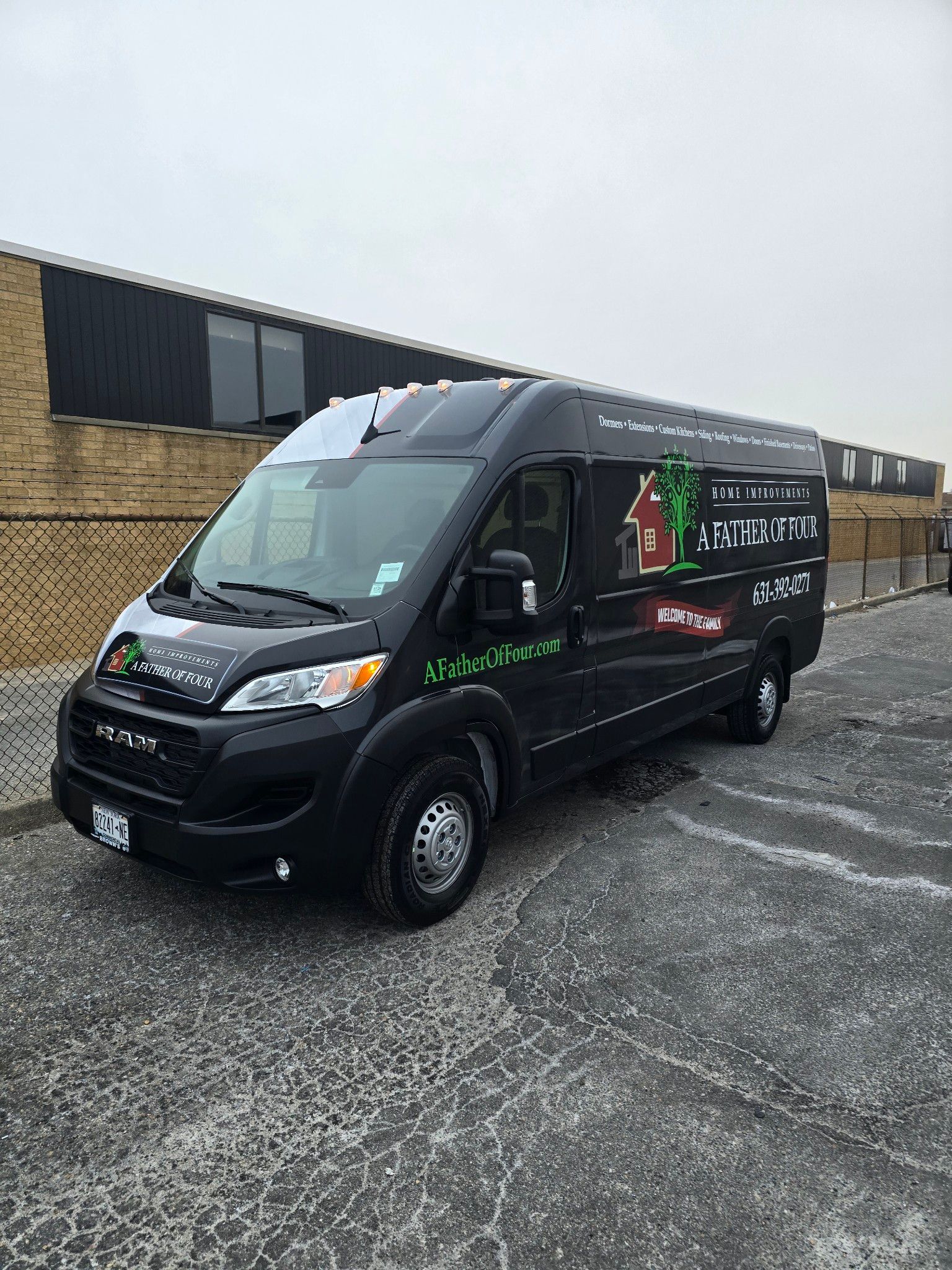 Black commercial van parked on a paved lot in front of a brick building.