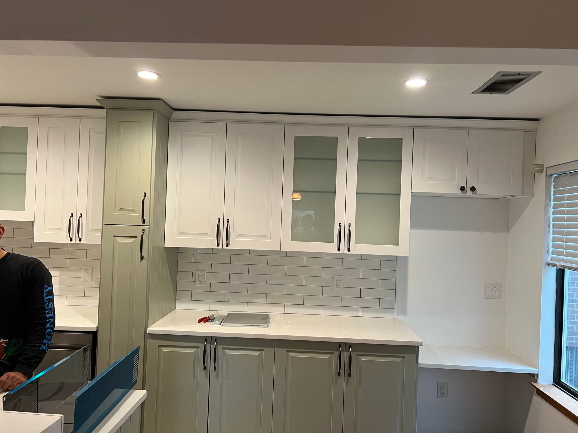 Kitchen with white and green cabinets, white countertops, and white and gray backsplash.