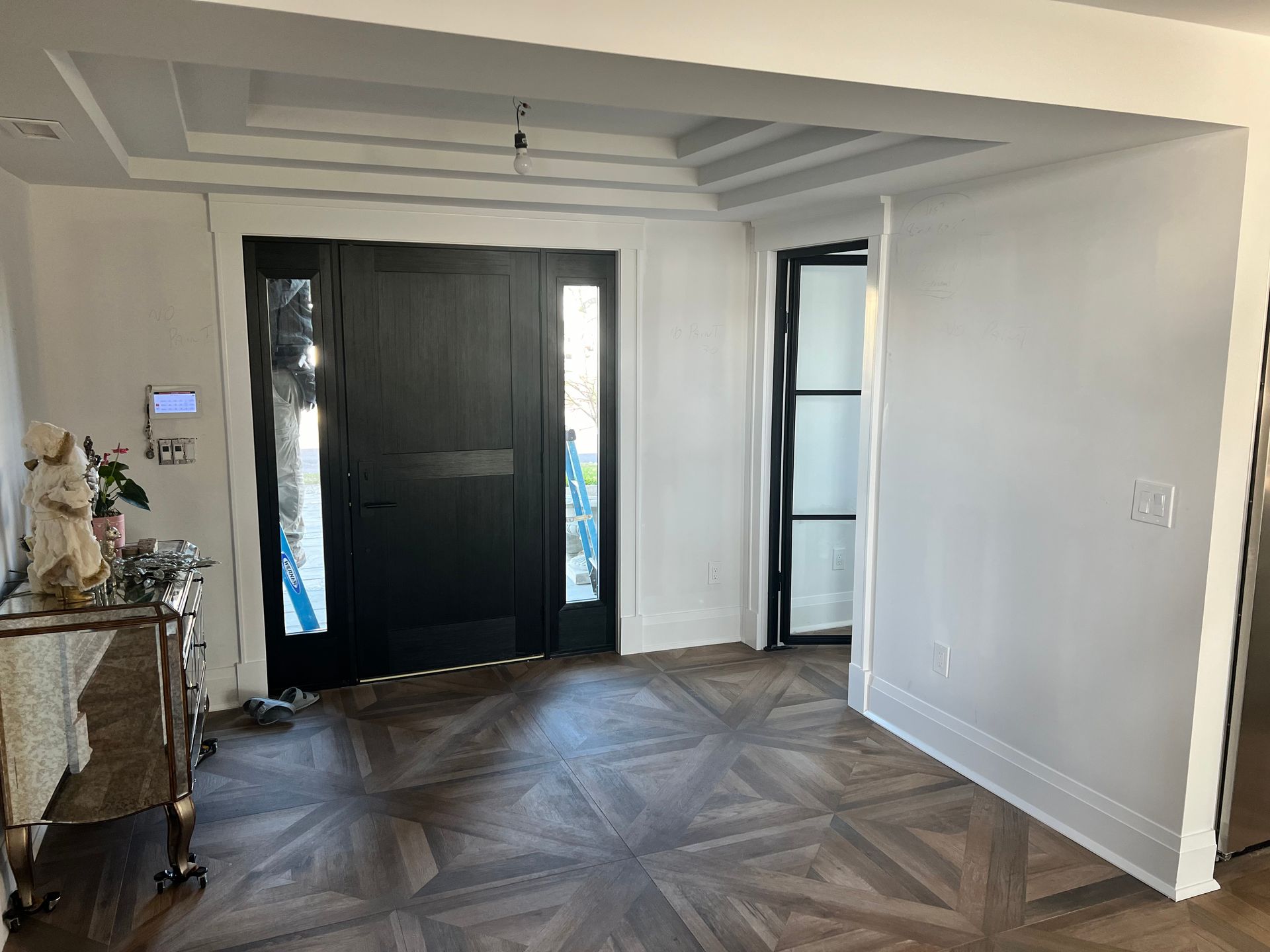 Elegant foyer with dark wood door, patterned floor, and white walls.