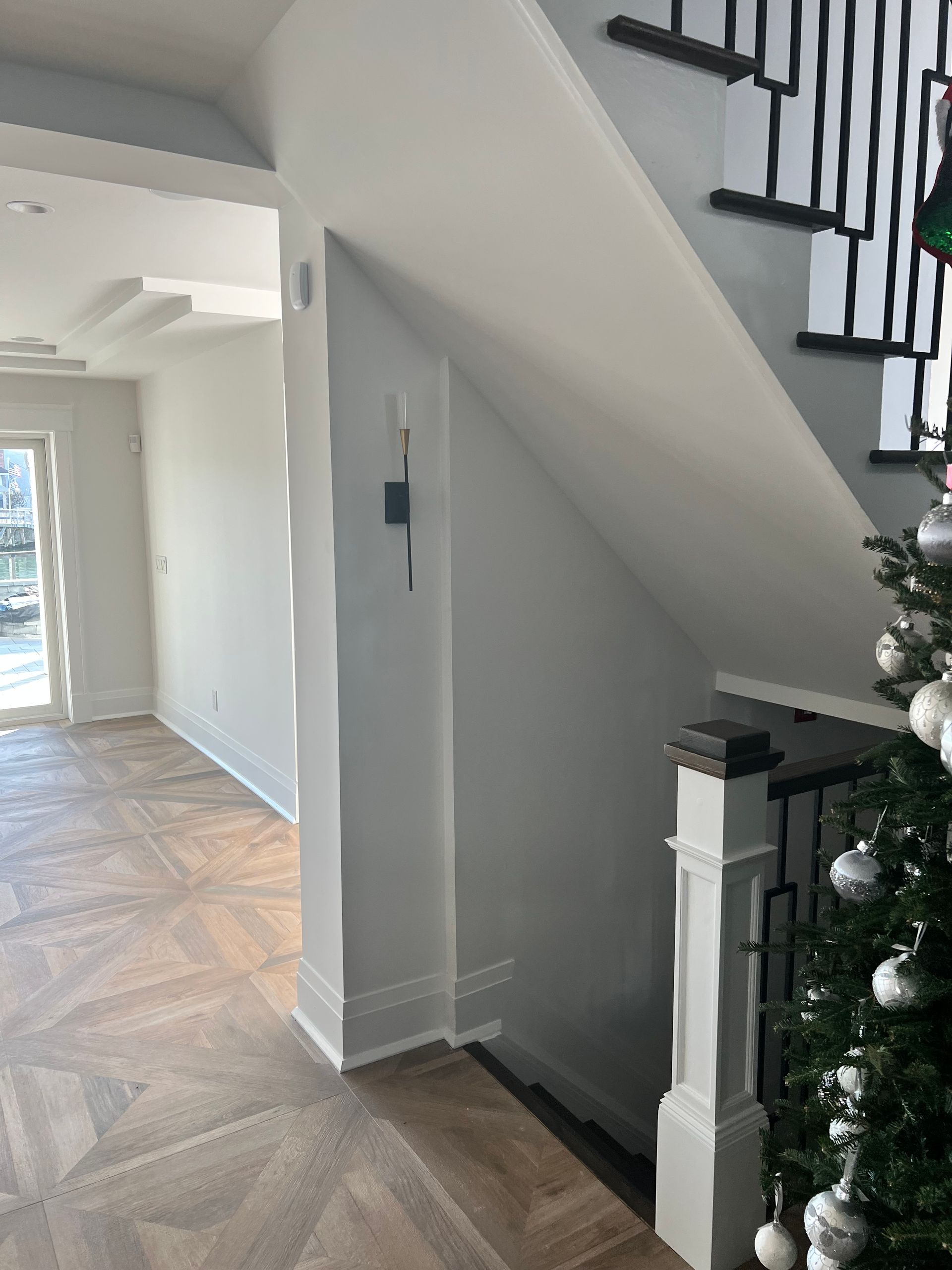 A staircase with black railings, next to a light-colored wall and wooden floor. A Christmas tree is visible.