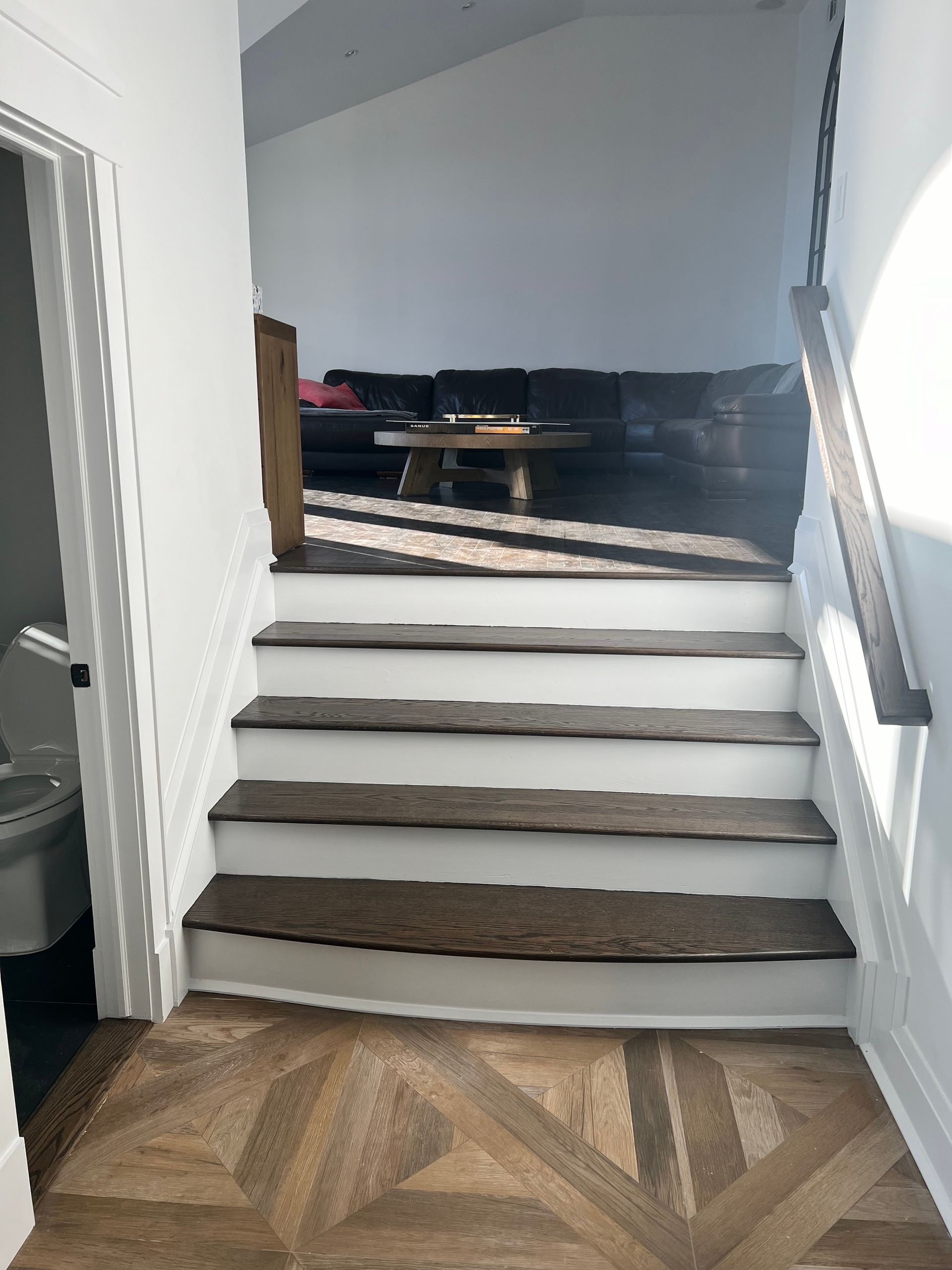 Staircase with wooden steps and a white trim leading up to a living room with a dark couch.