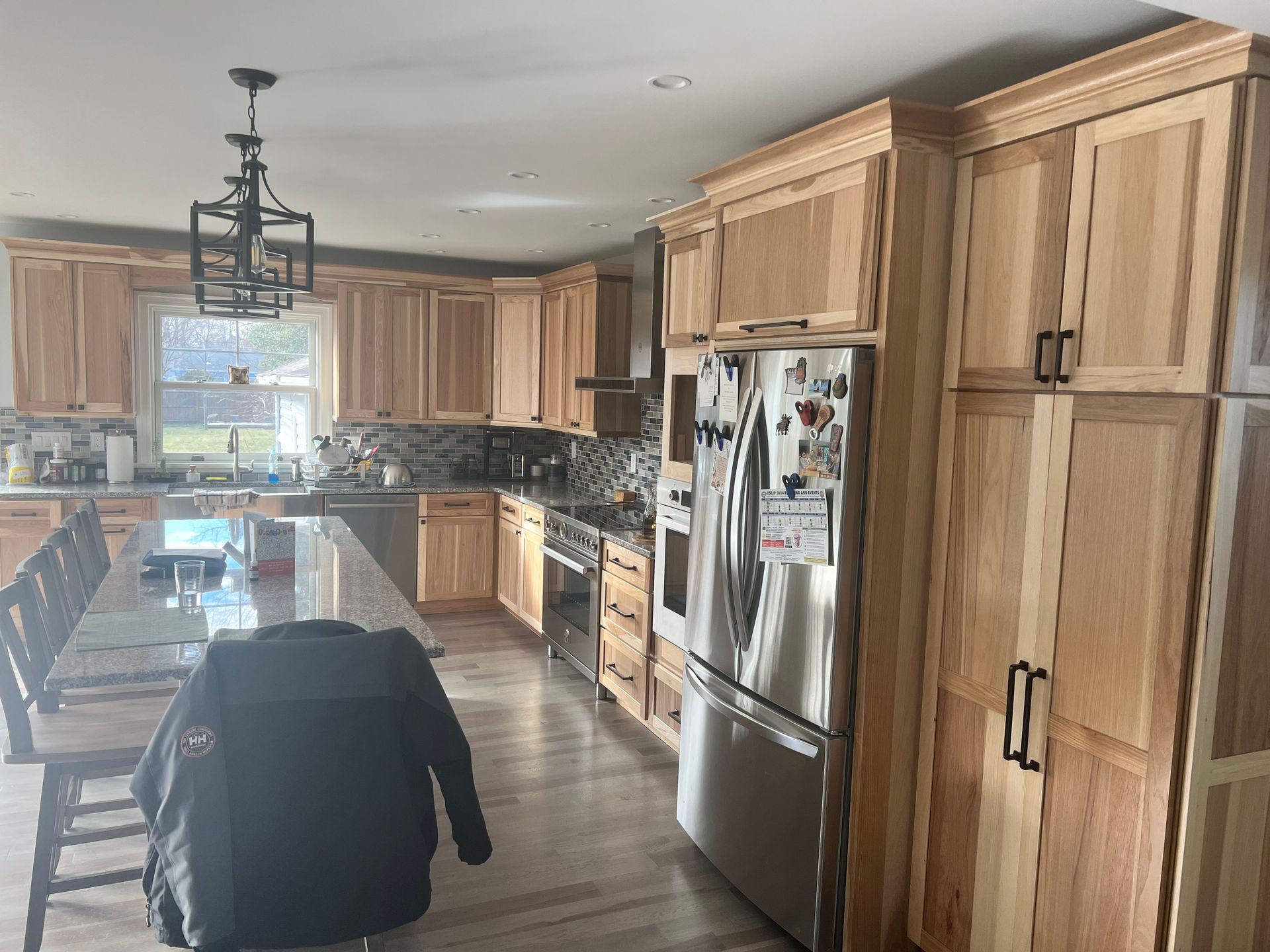 Kitchen with light wood cabinets, stainless steel appliances, and a granite island with a black jacket on a chair.