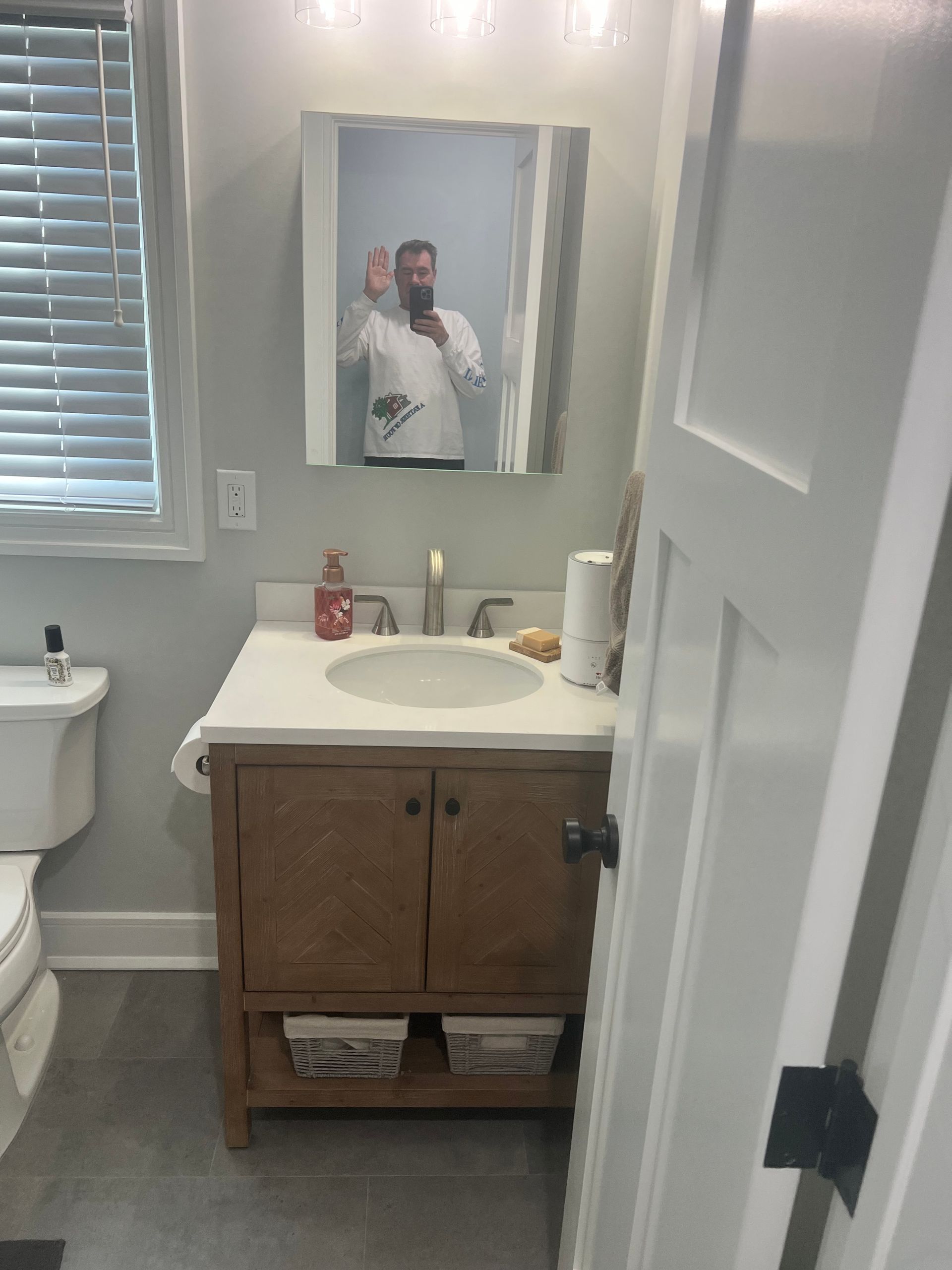 Bathroom with a wooden vanity, a white sink, and a person reflected in the mirror.