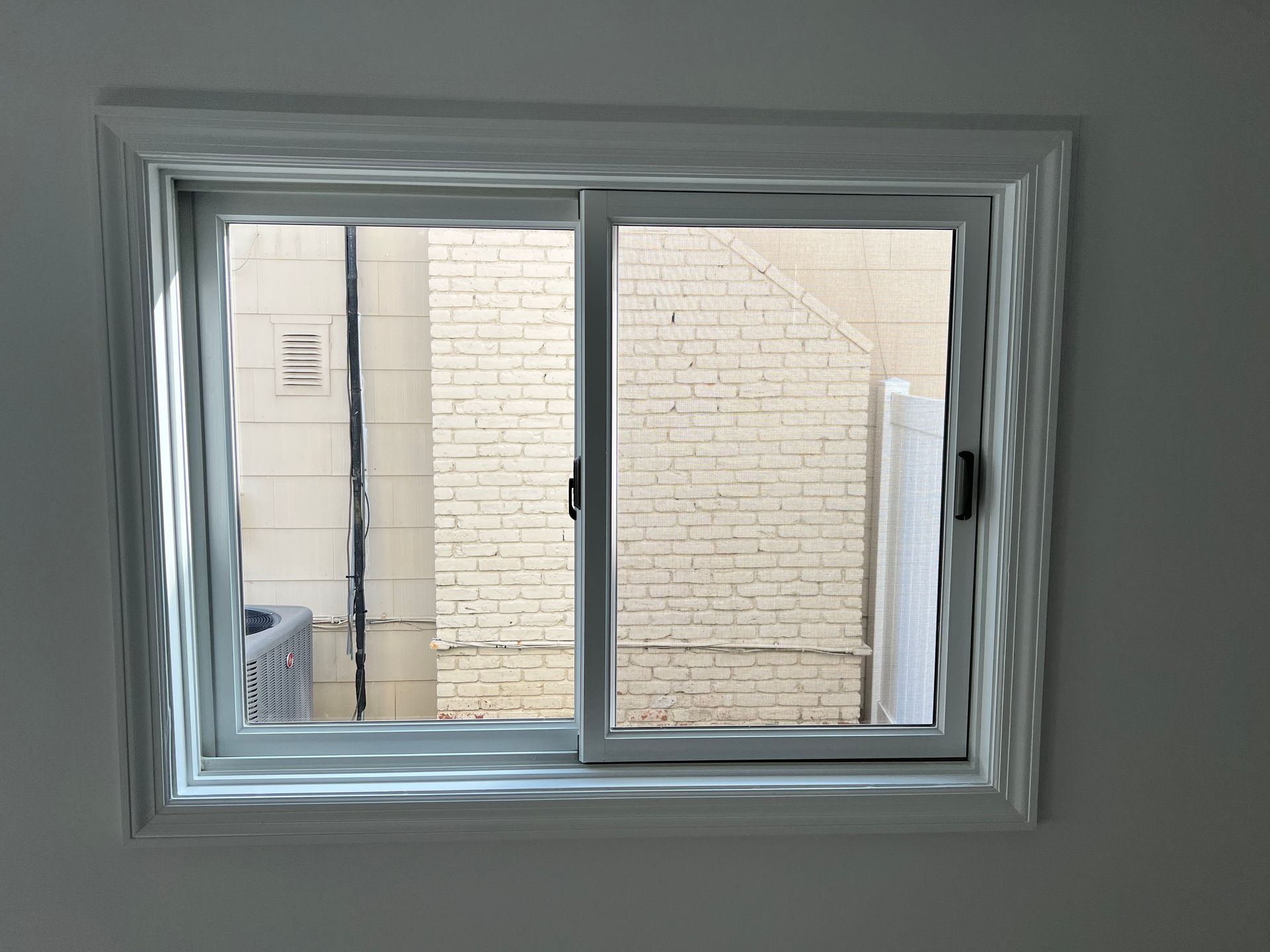 Sliding window with white frame, looking onto a brick wall and building exteriors.