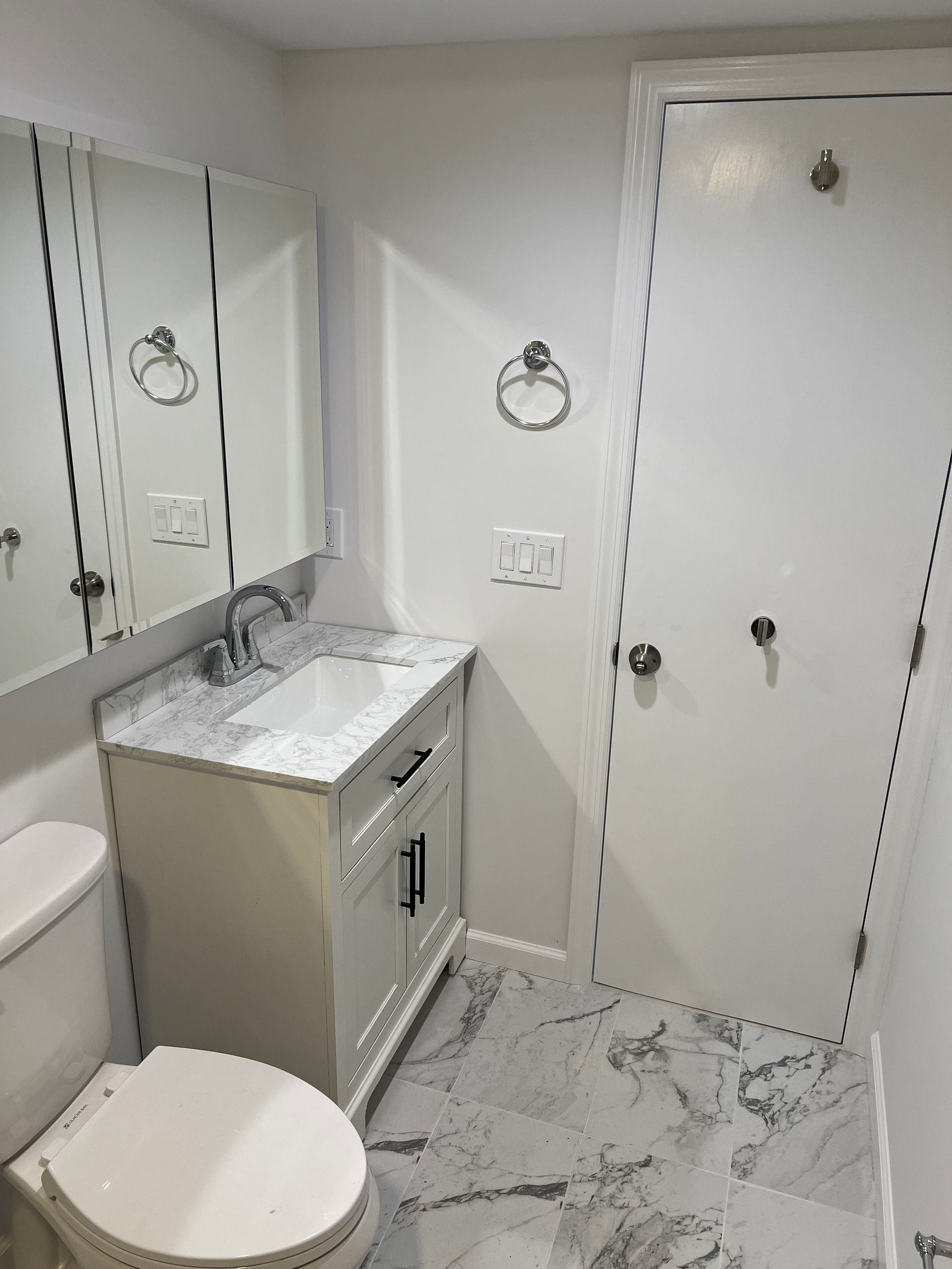 Bathroom with white vanity, marble-look floor, toilet, and mirrored medicine cabinet.