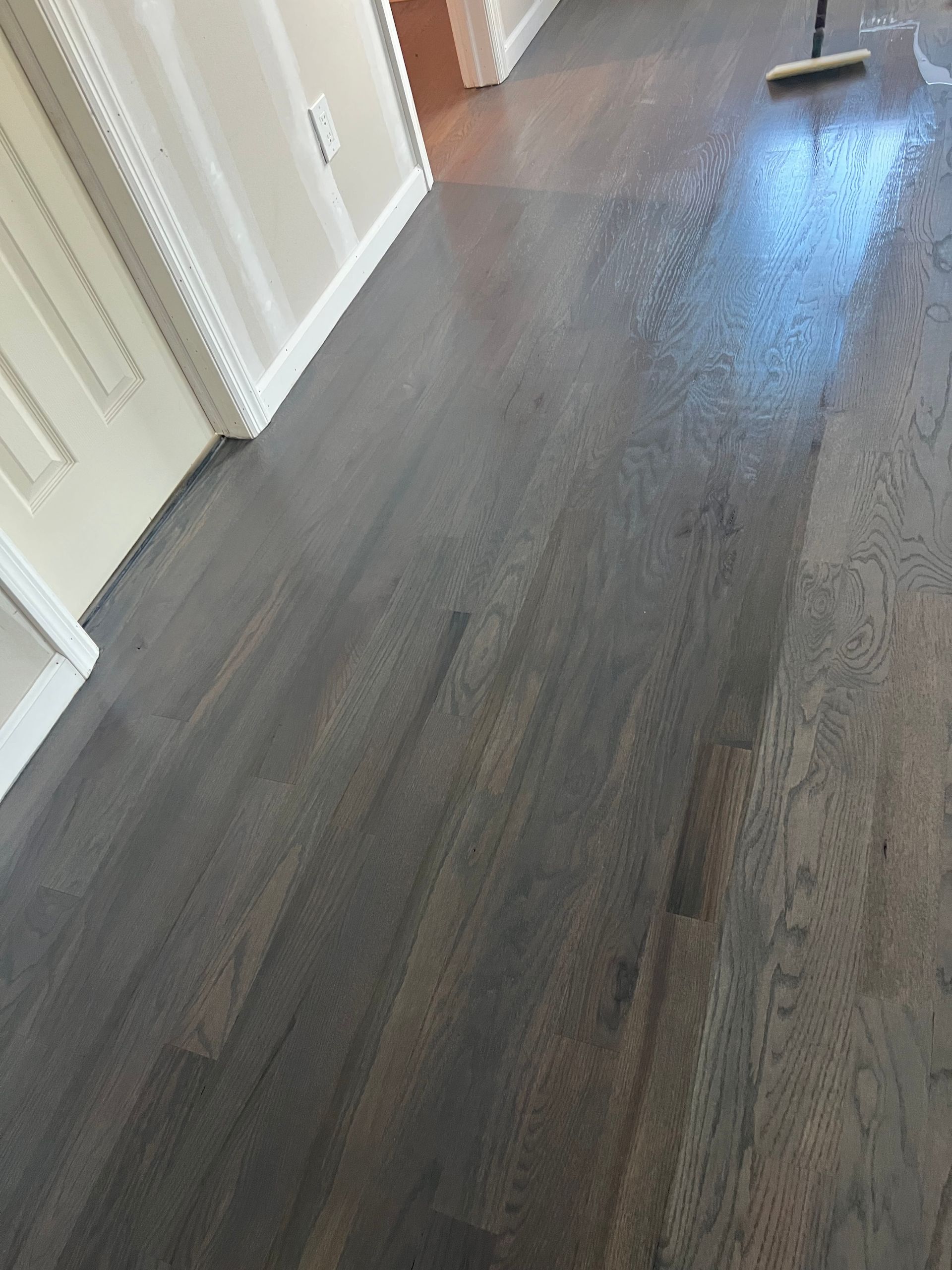 Dark stained hardwood floor in a hallway, wet from cleaning. A mop handle is visible.