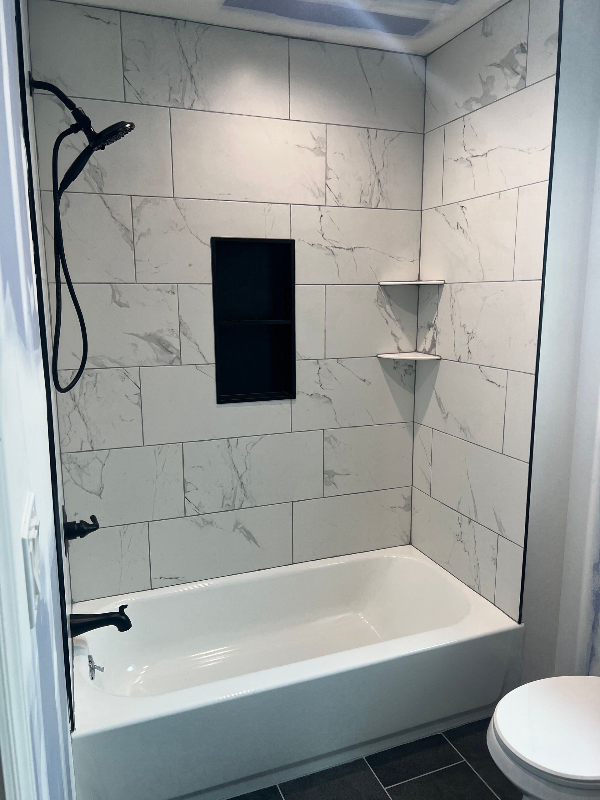 Bathroom with white marble-look tiles, black shower fixtures, tub, and toilet.