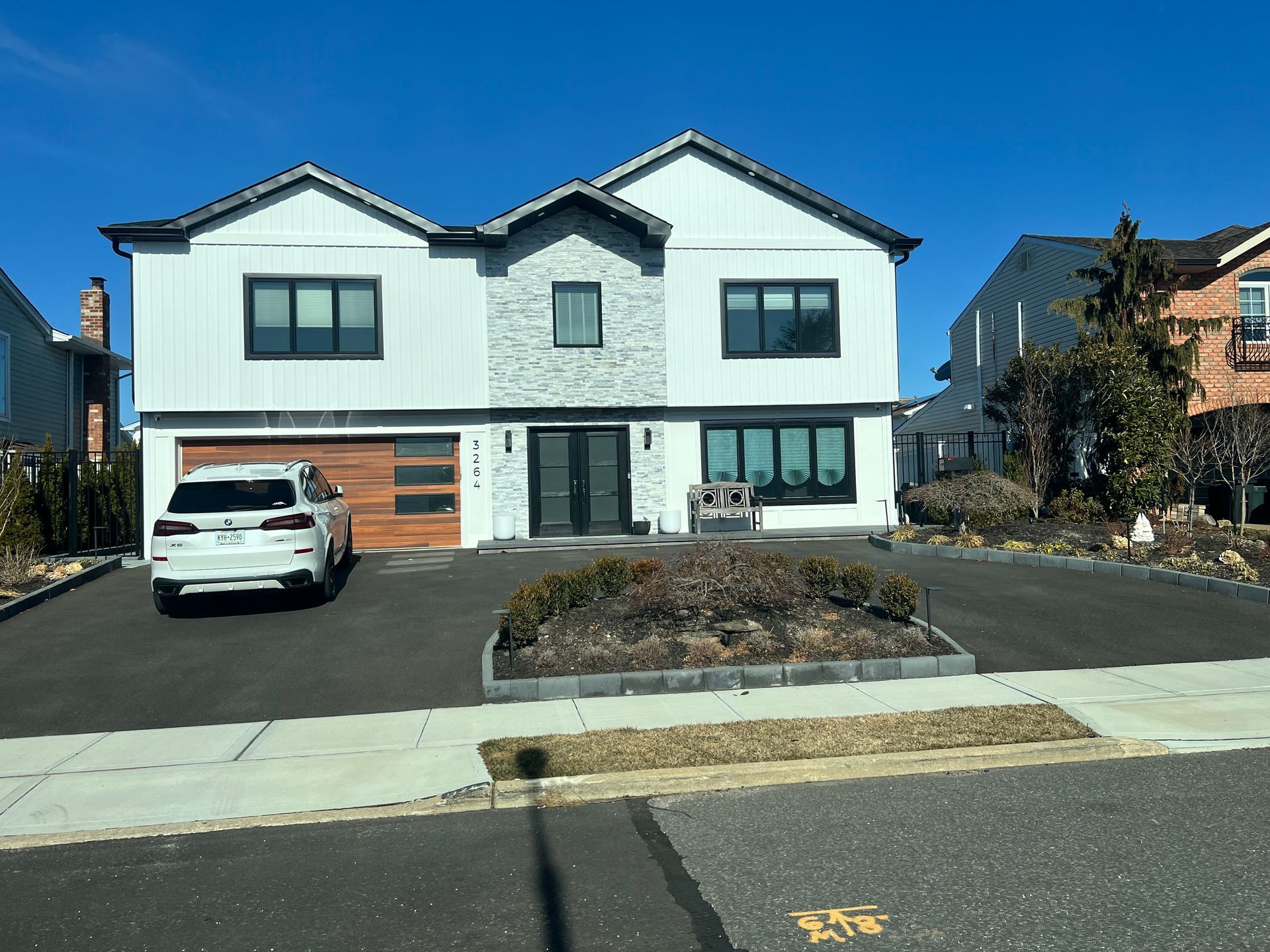 Modern white two-story house with black trim, a stone accent, and a wood garage door.