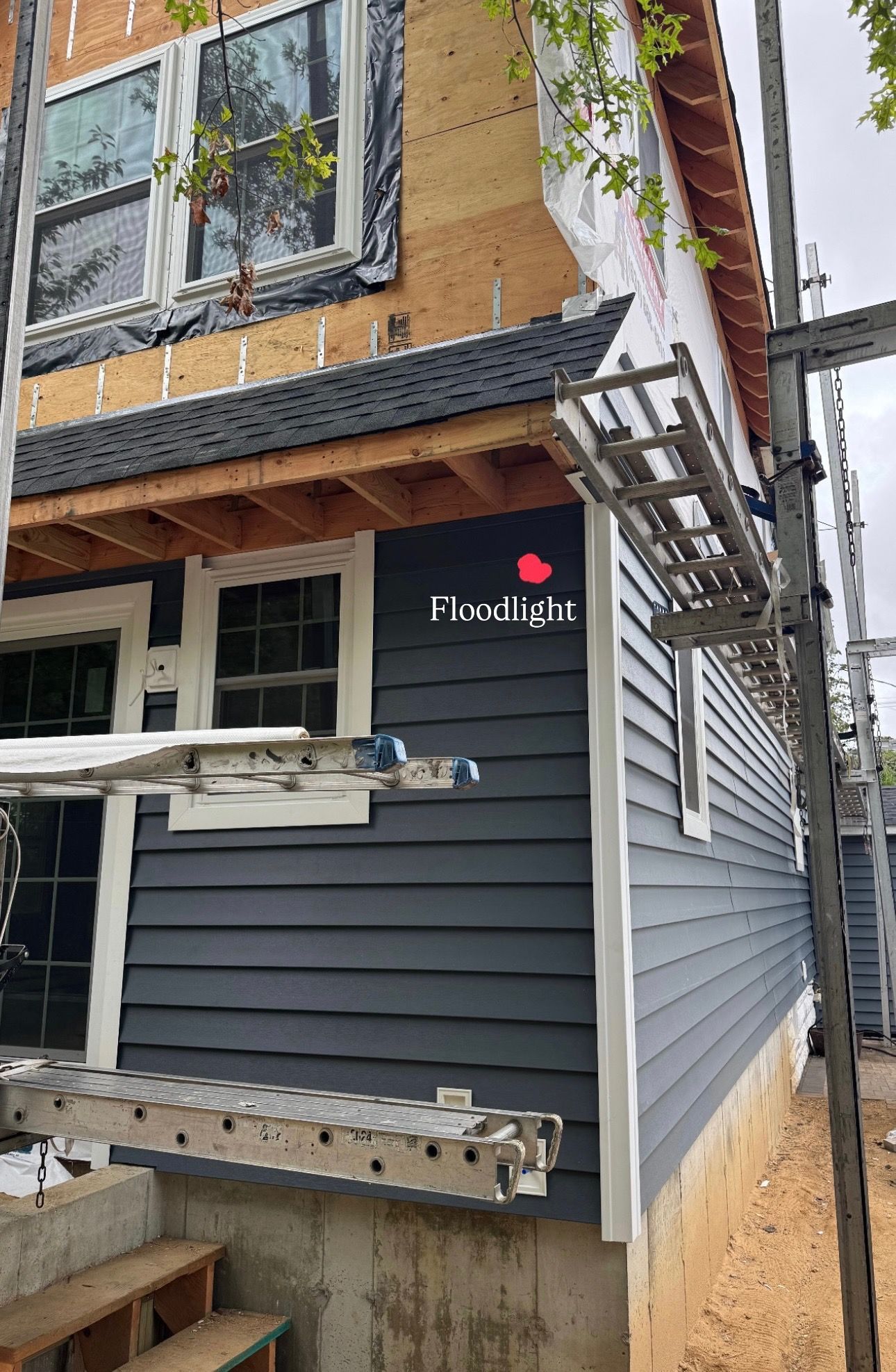 Construction of a house with dark blue siding, a Floodlight logo, and scaffolding.