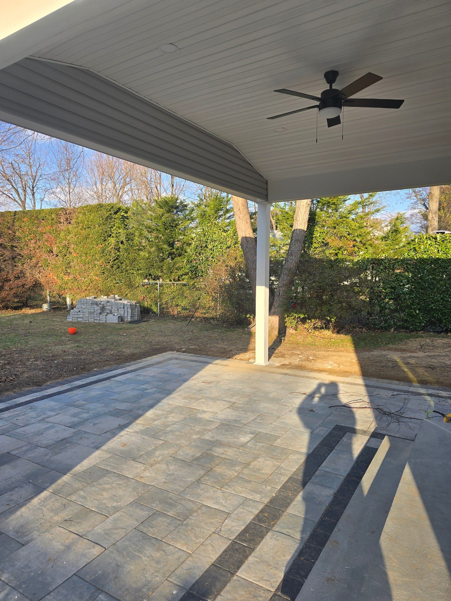 Covered patio with a ceiling fan, overlooking a yard with landscaping. Shadows cast by the sun.