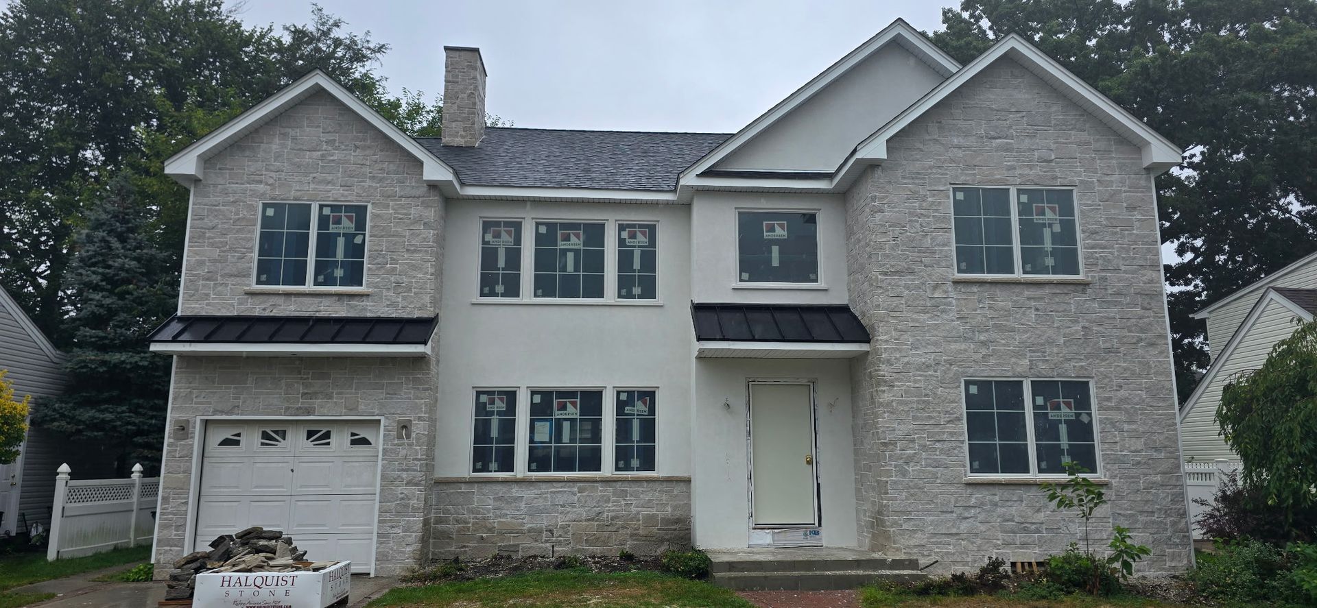 Two-story house under construction, featuring light stone and white siding. New windows, garage door, and a black roof.