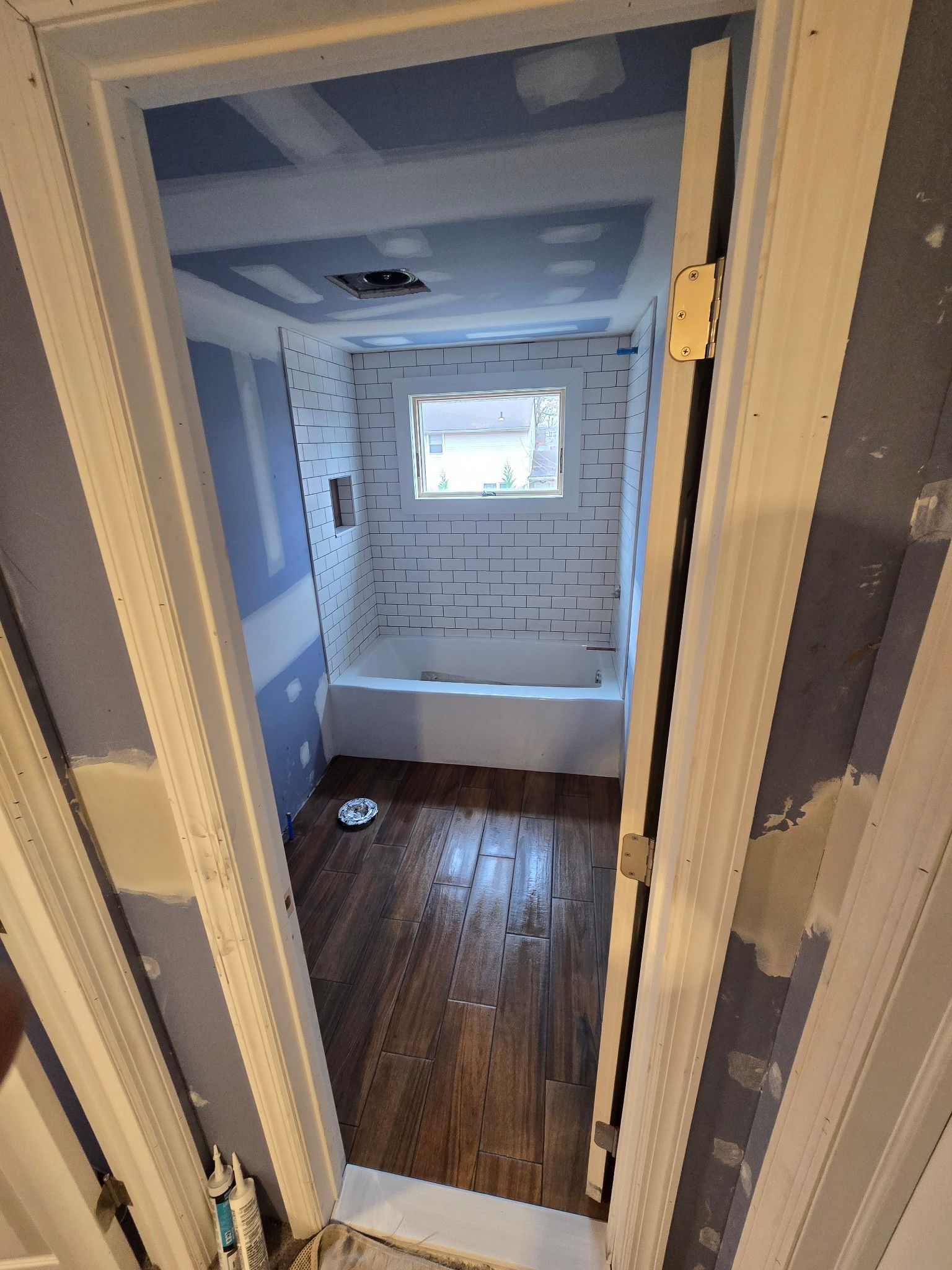 Bathroom under construction with blue drywall, white tile, and wood floor.