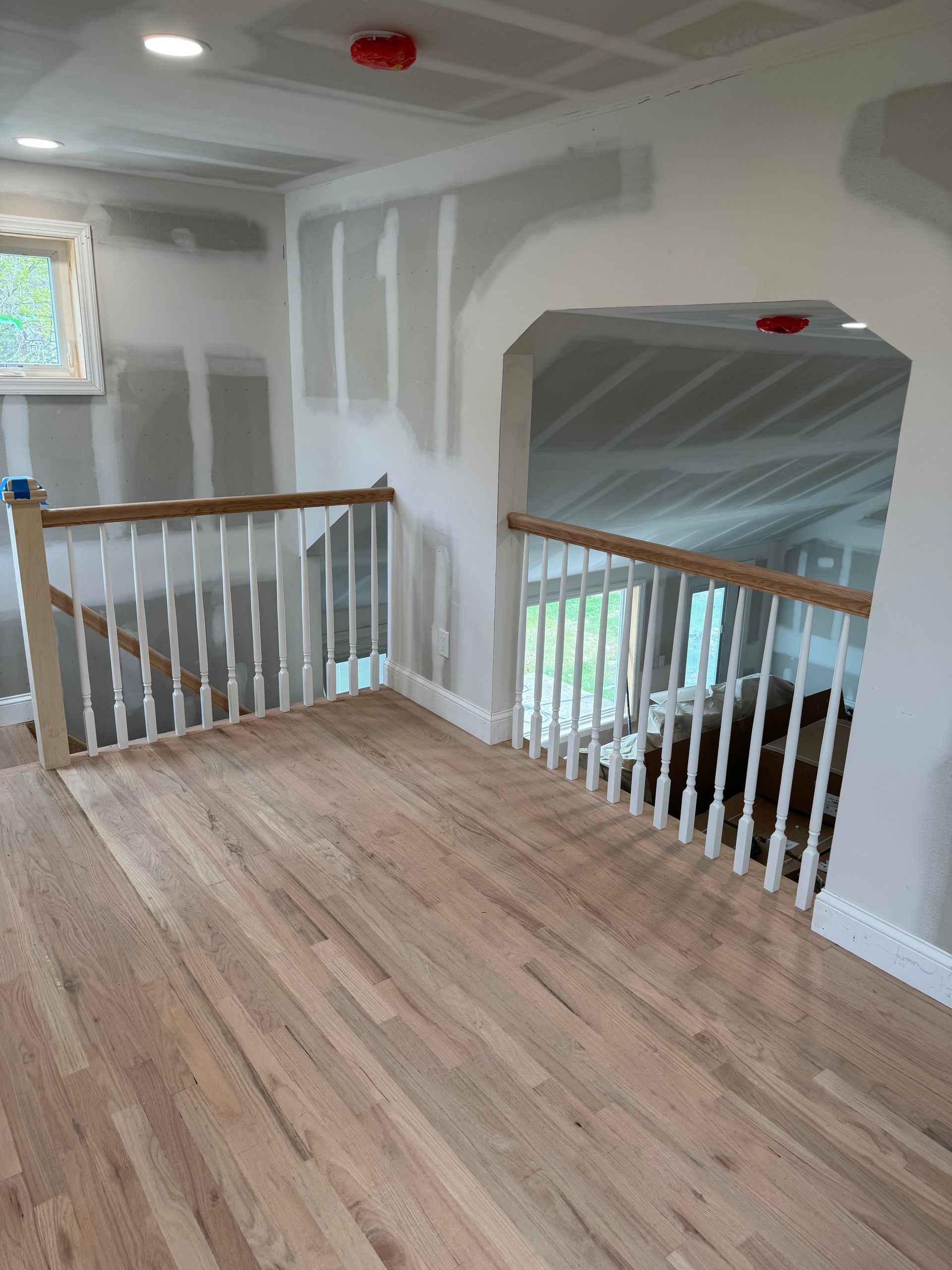 Interior with hardwood floors, stairs, and unfinished drywall. White railing with wooden handrail.