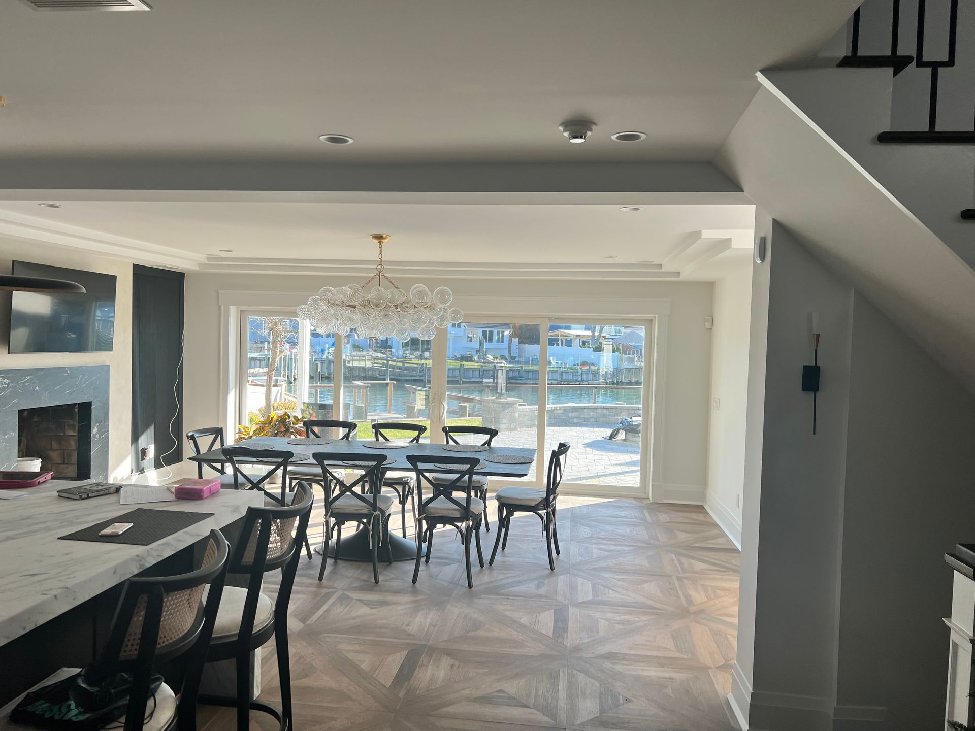 Dining room with a chandelier, large window overlooking water, and a wooden floor.