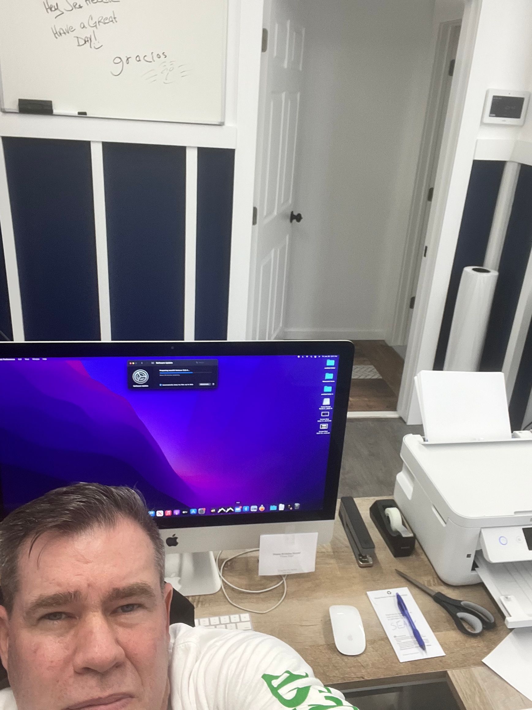 Man at desk with computer, printer, and whiteboard. Office setting. Purple screen.