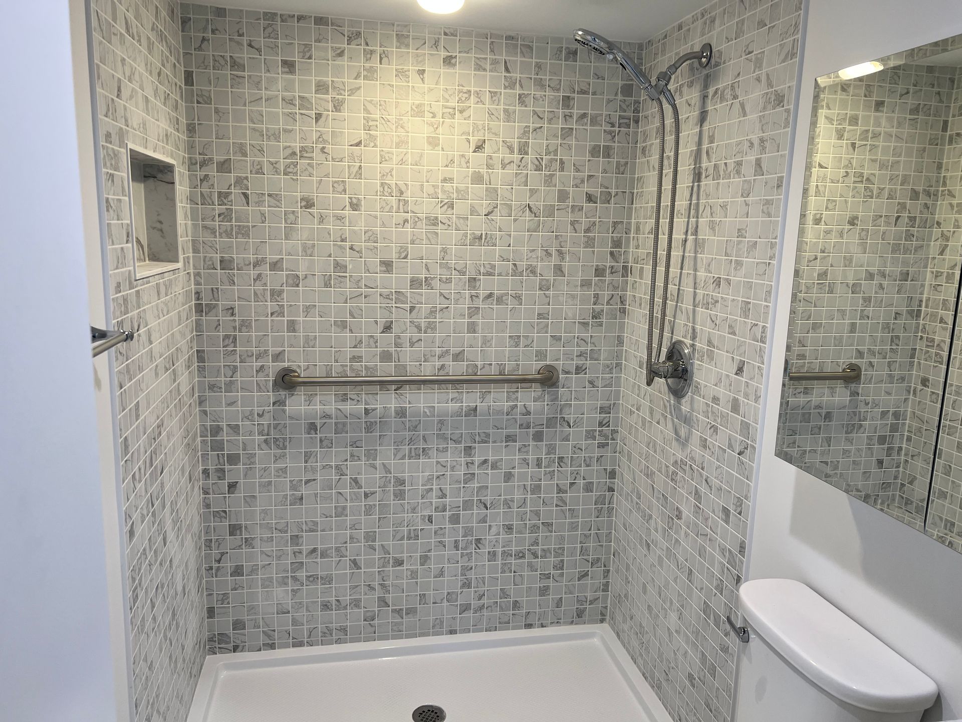 Accessible bathroom with gray tiled walls, grab bar, showerhead, and toilet.