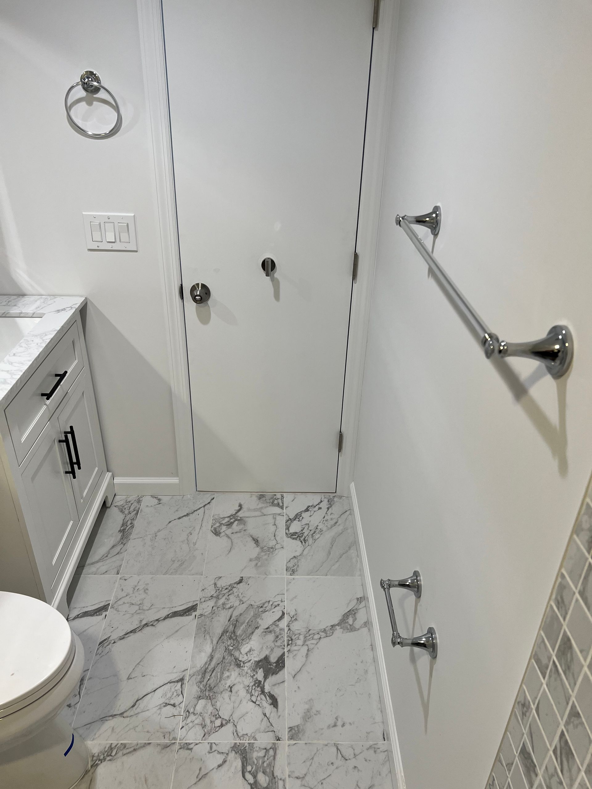 Bathroom with white walls, marble-look floor tile, and chrome fixtures: towel bar, toilet paper ring, towel hooks.
