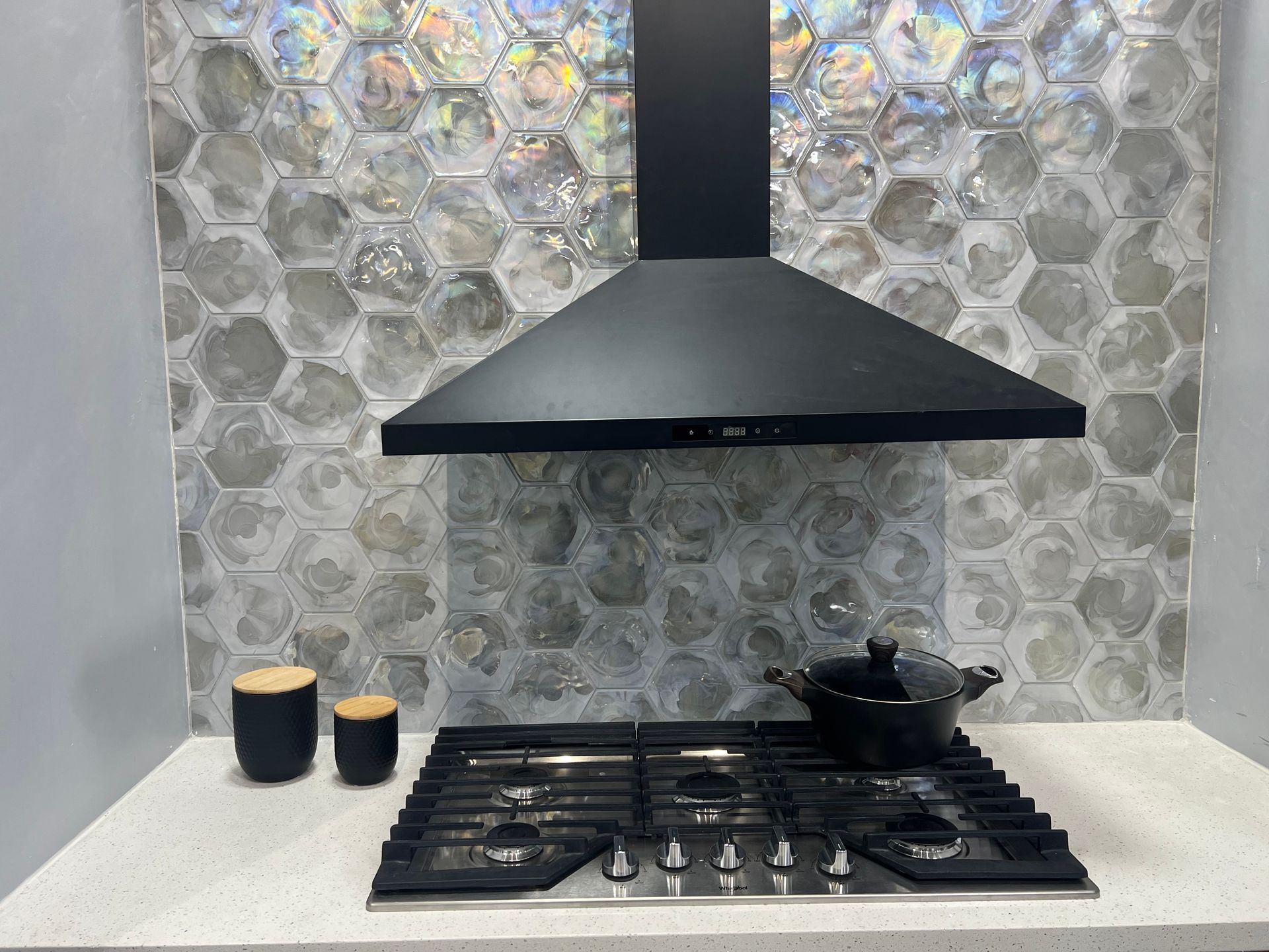 Kitchen with black range hood, gas cooktop, and hexagonal gray backsplash.