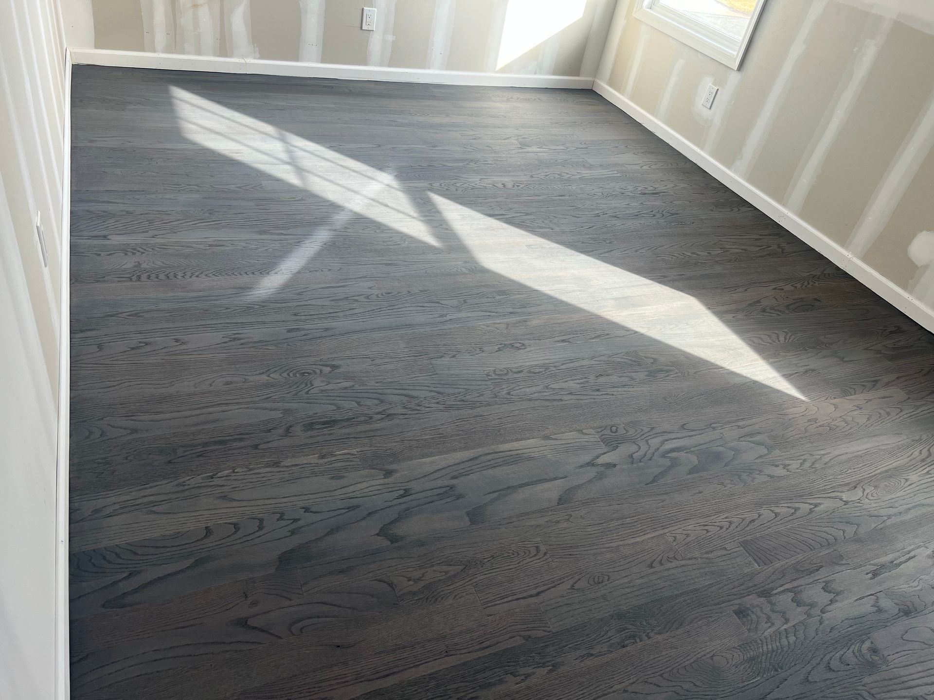 Gray-stained hardwood floor in an unfinished room, with sunlight creating a bright angular pattern.