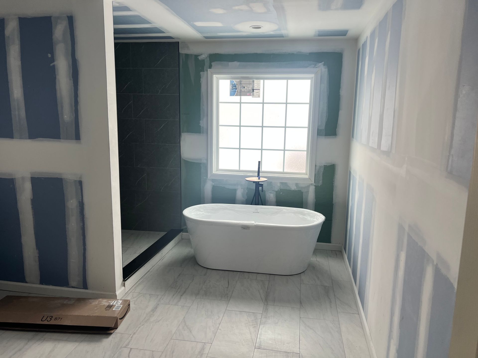 Bathroom under construction with bathtub, window, and drywall.