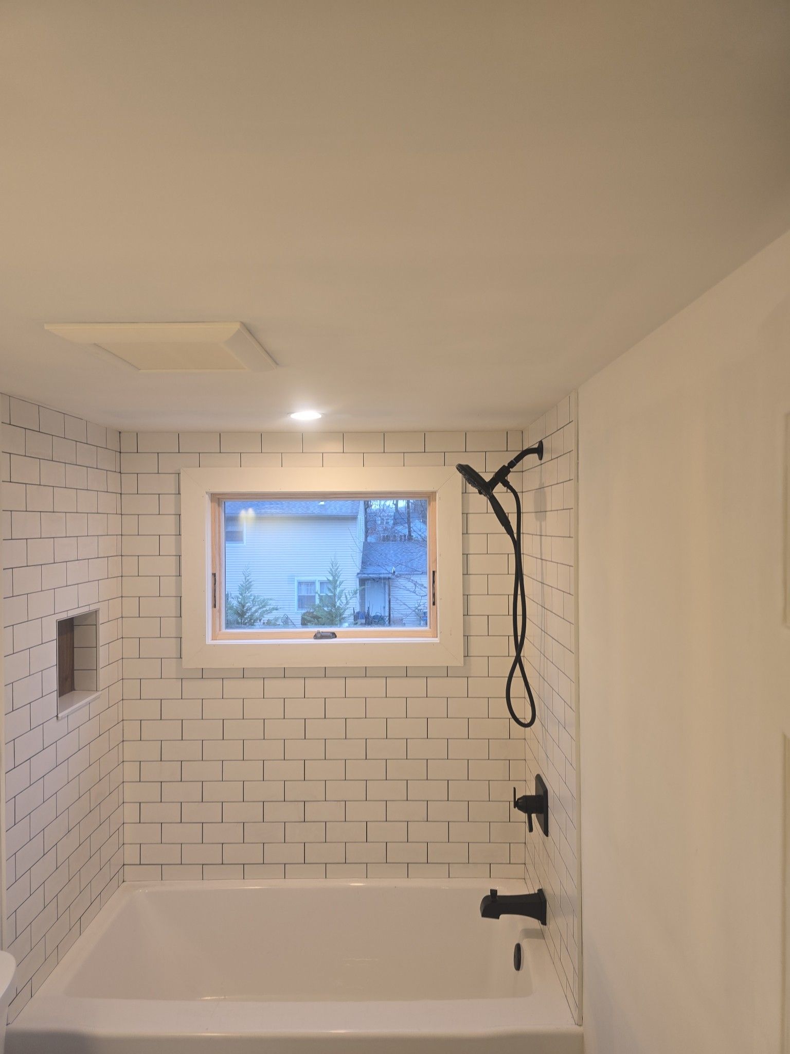 Bathroom with white tub, black shower fixtures, and window with small tree visible.