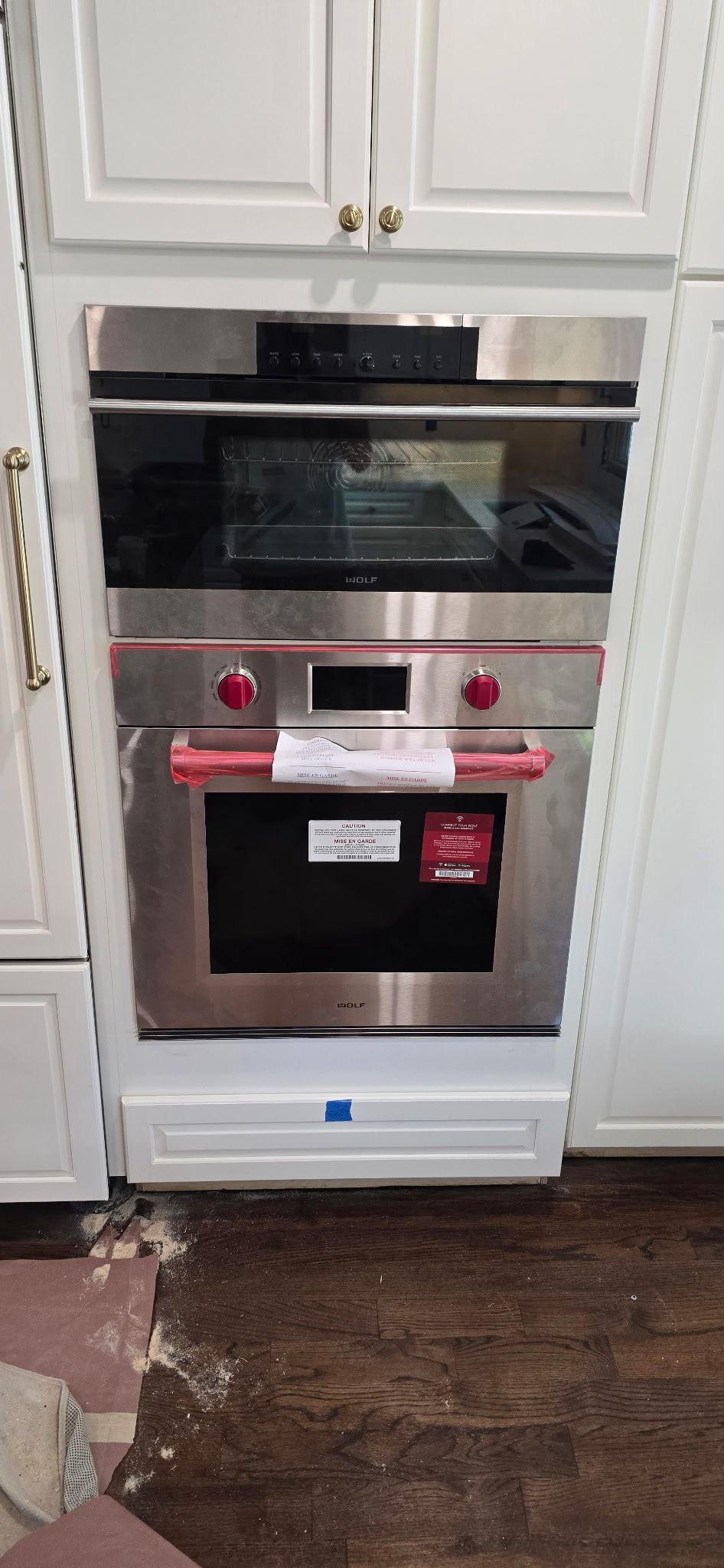 Stainless steel double oven built into white cabinets. Red knobs.