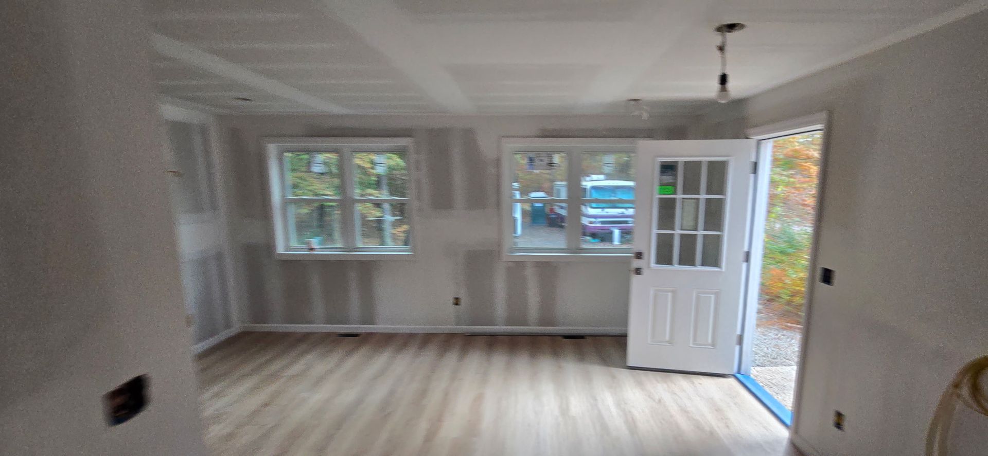 Interior of a room under construction with new windows, a door, and wood flooring.