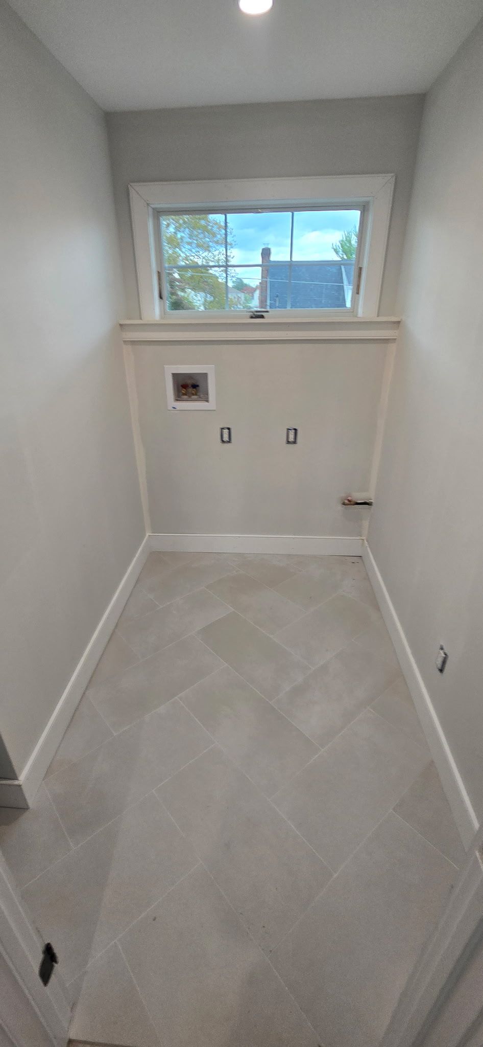 Empty laundry room with a window, white walls, and gray flooring.