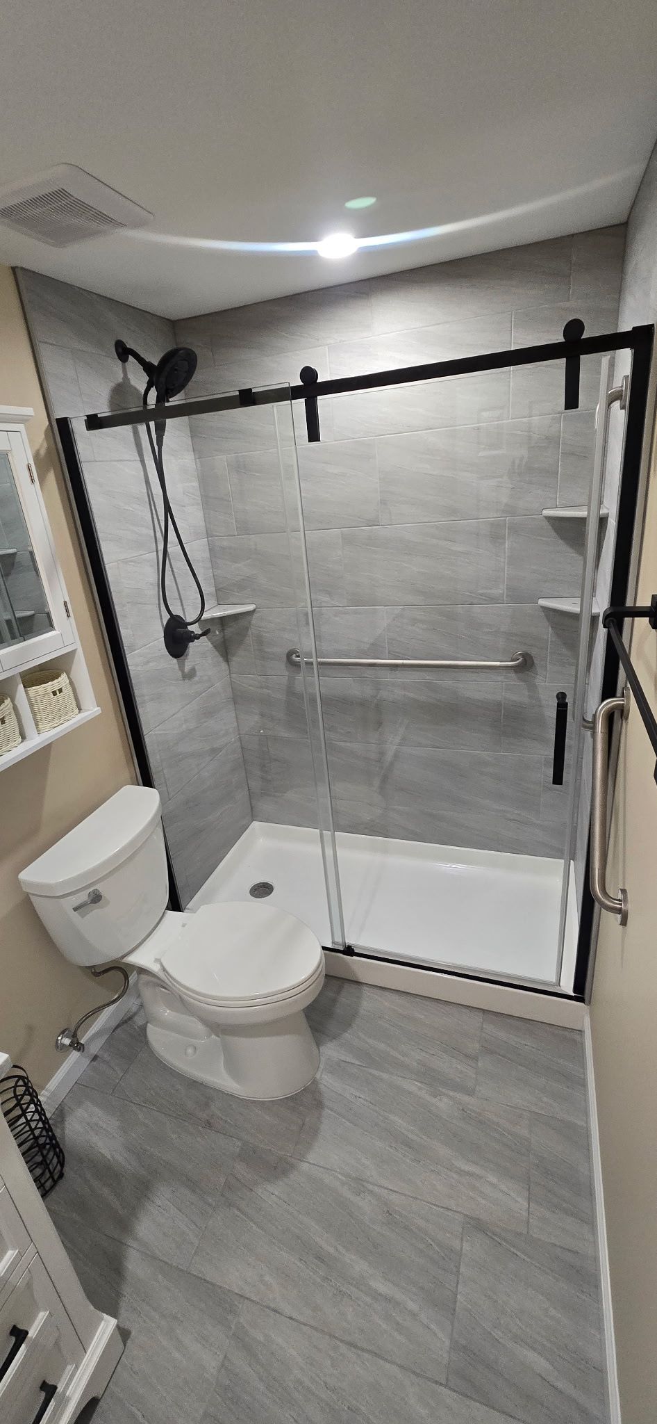 Bathroom with gray tiled shower and floor, black shower door frame, and white toilet.