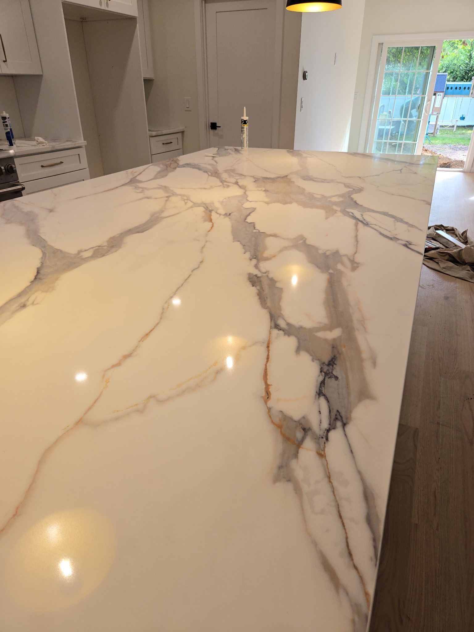 White and gold veined countertop in a kitchen with a sink faucet and sliding glass doors.