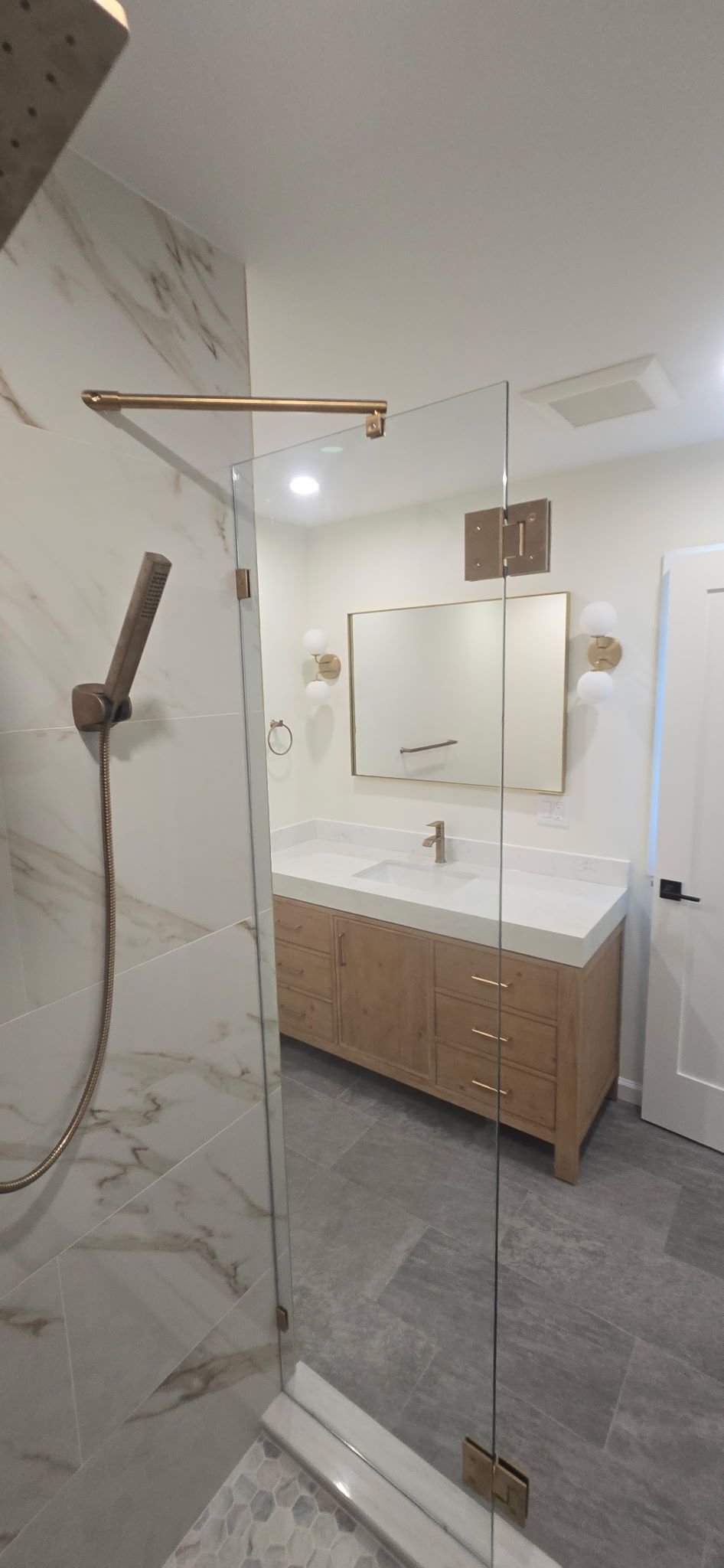 A modern bathroom with marble walls and flooring, a glass shower door, and a wooden vanity.
