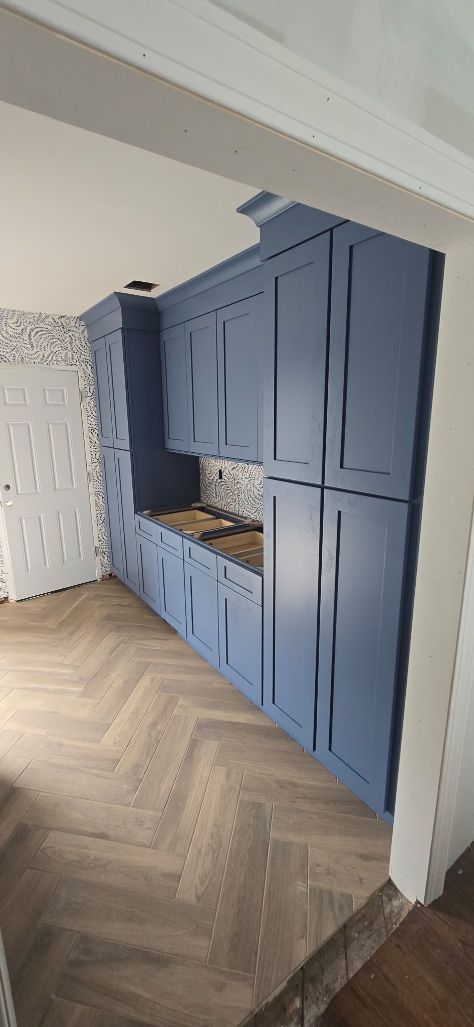 Blue kitchen cabinets with tile backsplash and herringbone patterned wood floor.
