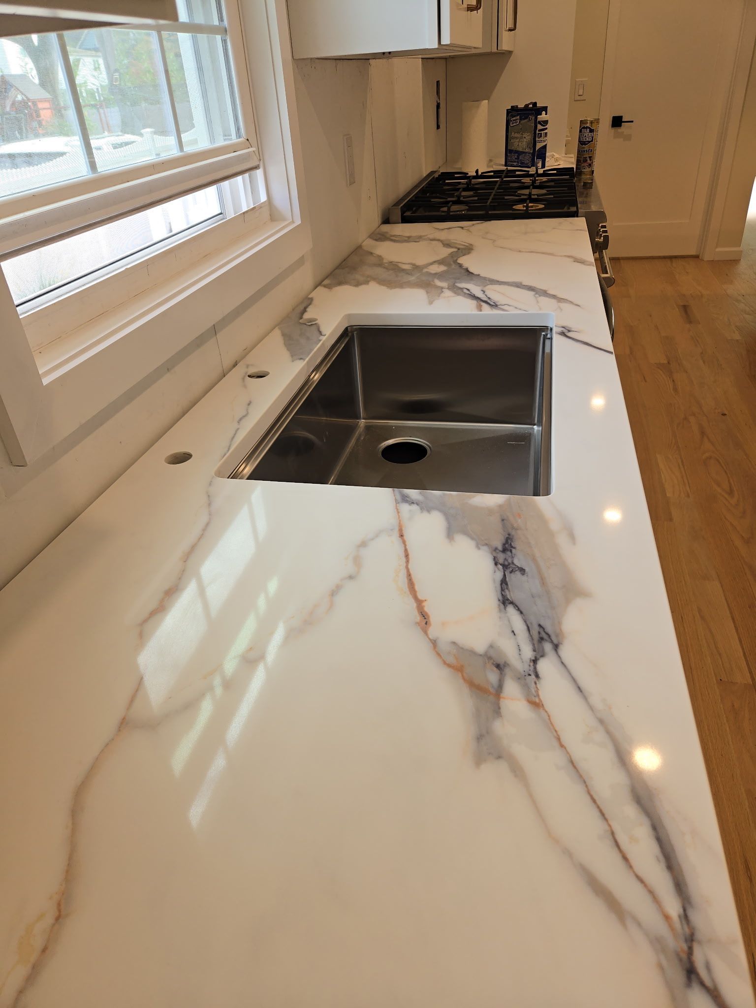 White marble countertop with veining, stainless steel sink, and a window in a kitchen.