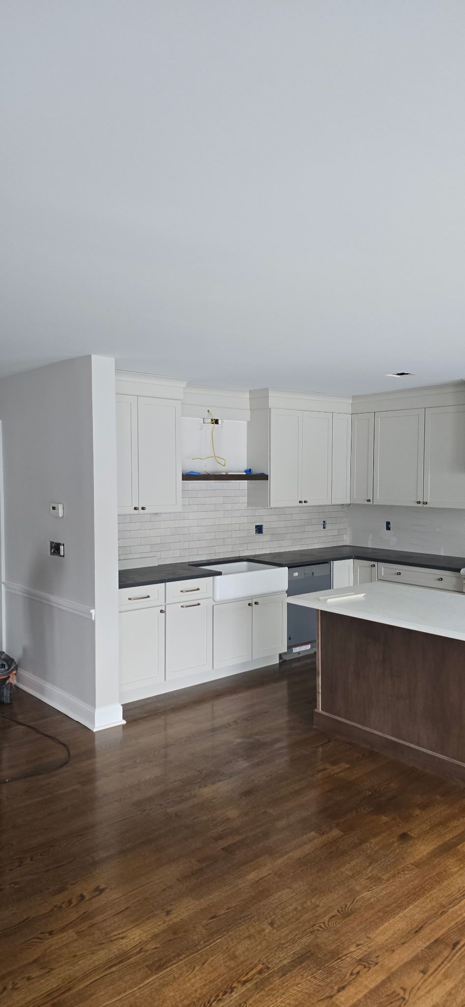 A kitchen with white cabinets, dark countertops, and a wooden floor.