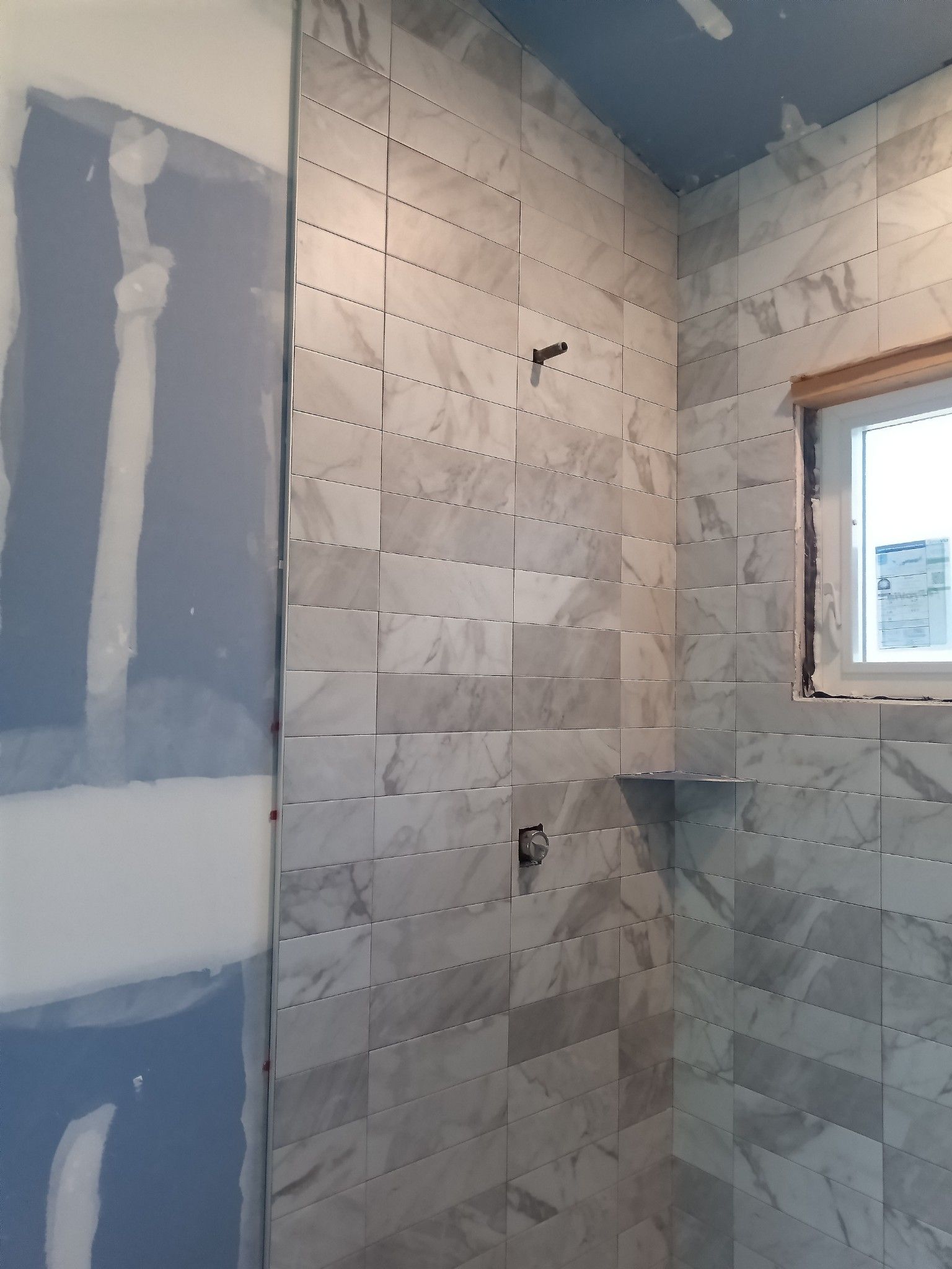 Shower walls tiled in gray marble, partially built. Drywall is visible on the left.