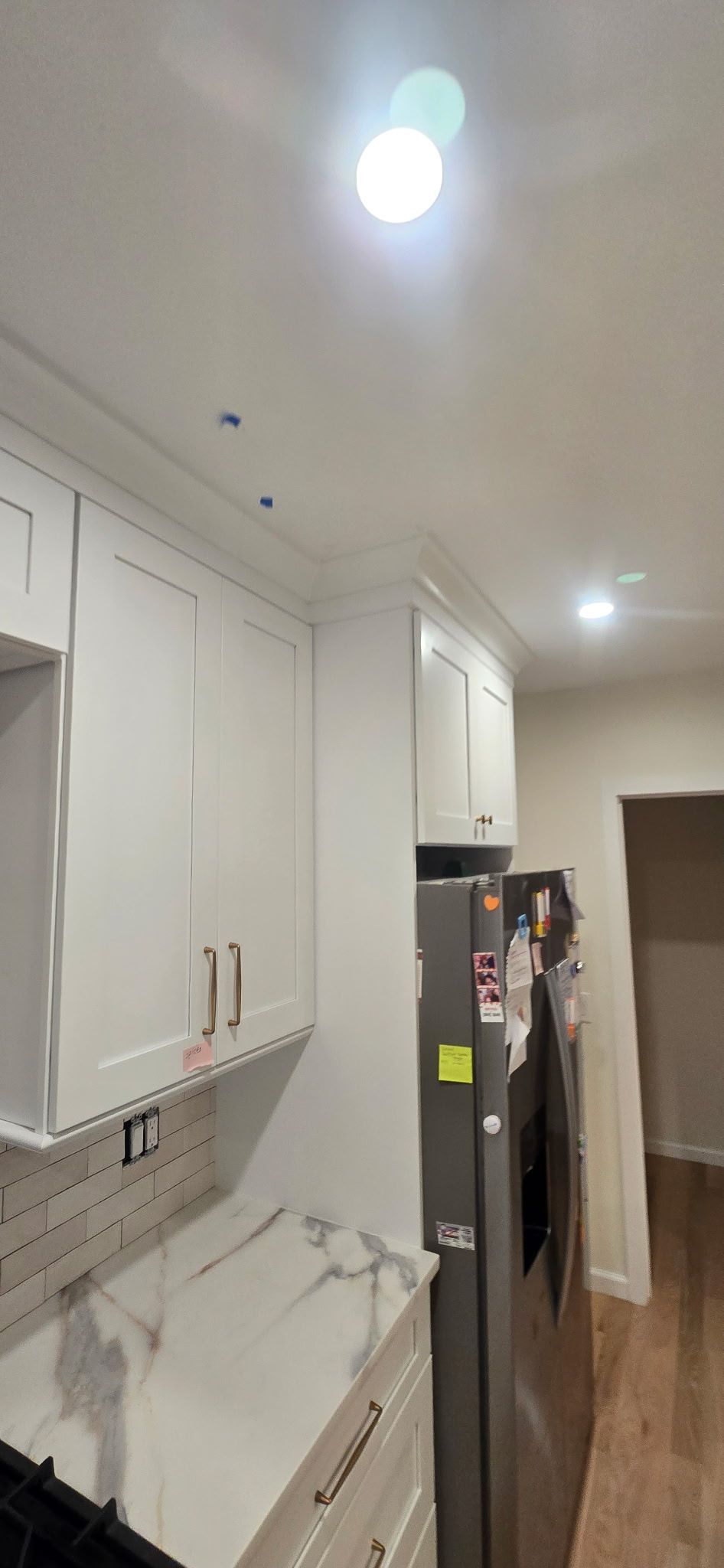 Kitchen with white cabinets, marble countertop, stainless steel refrigerator, and recessed lighting.