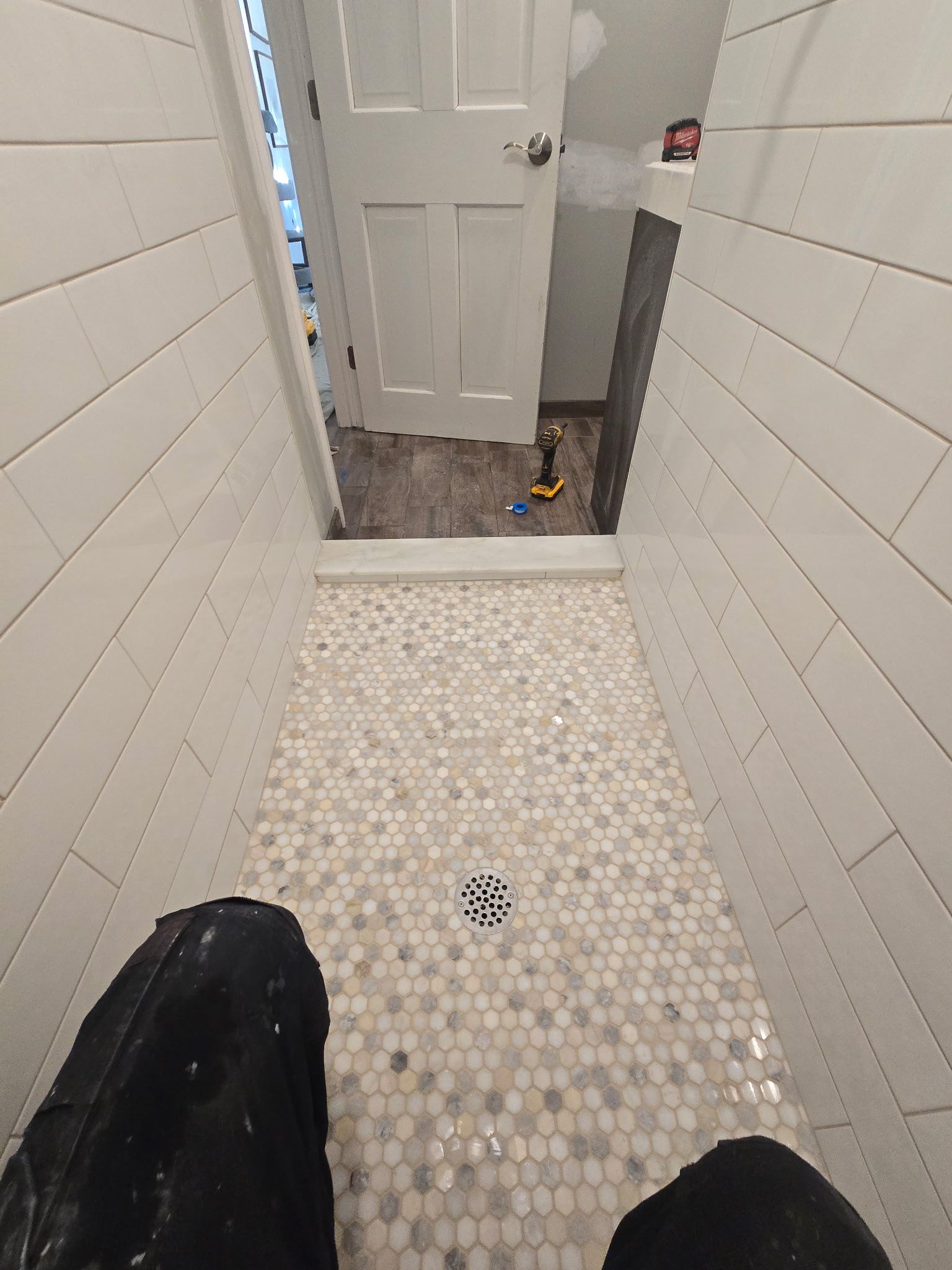 A newly tiled shower with white and gray mosaic tile floor and white plank walls, view from the feet.