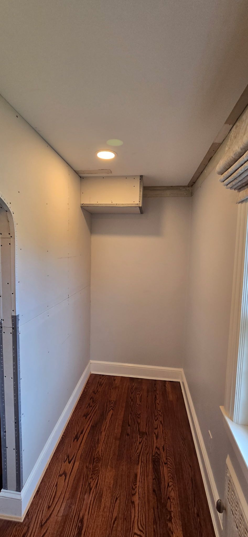 A narrow hallway with hardwood floors, light gray walls, and a recessed ceiling light.