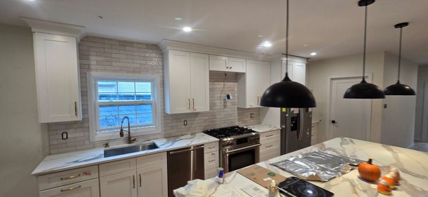Newly renovated kitchen with white cabinets, tile backsplash, and black pendant lights.