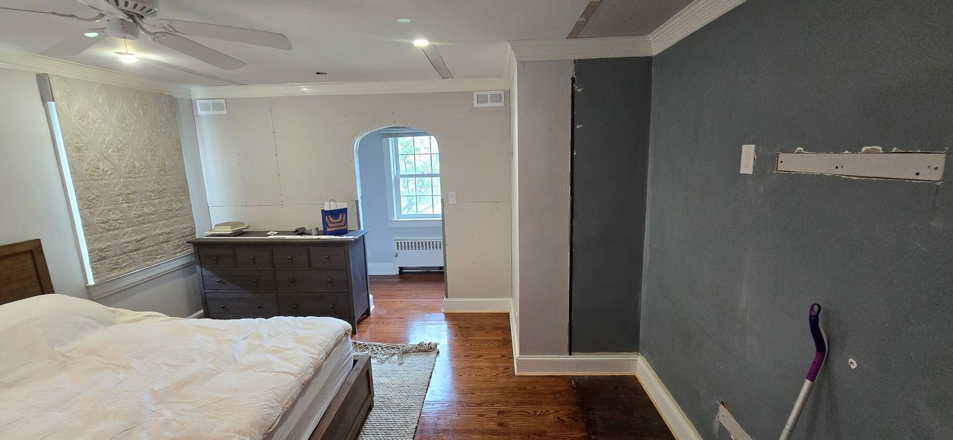 Bedroom interior with gray walls, wood floors, bed, dresser, and arched doorway.