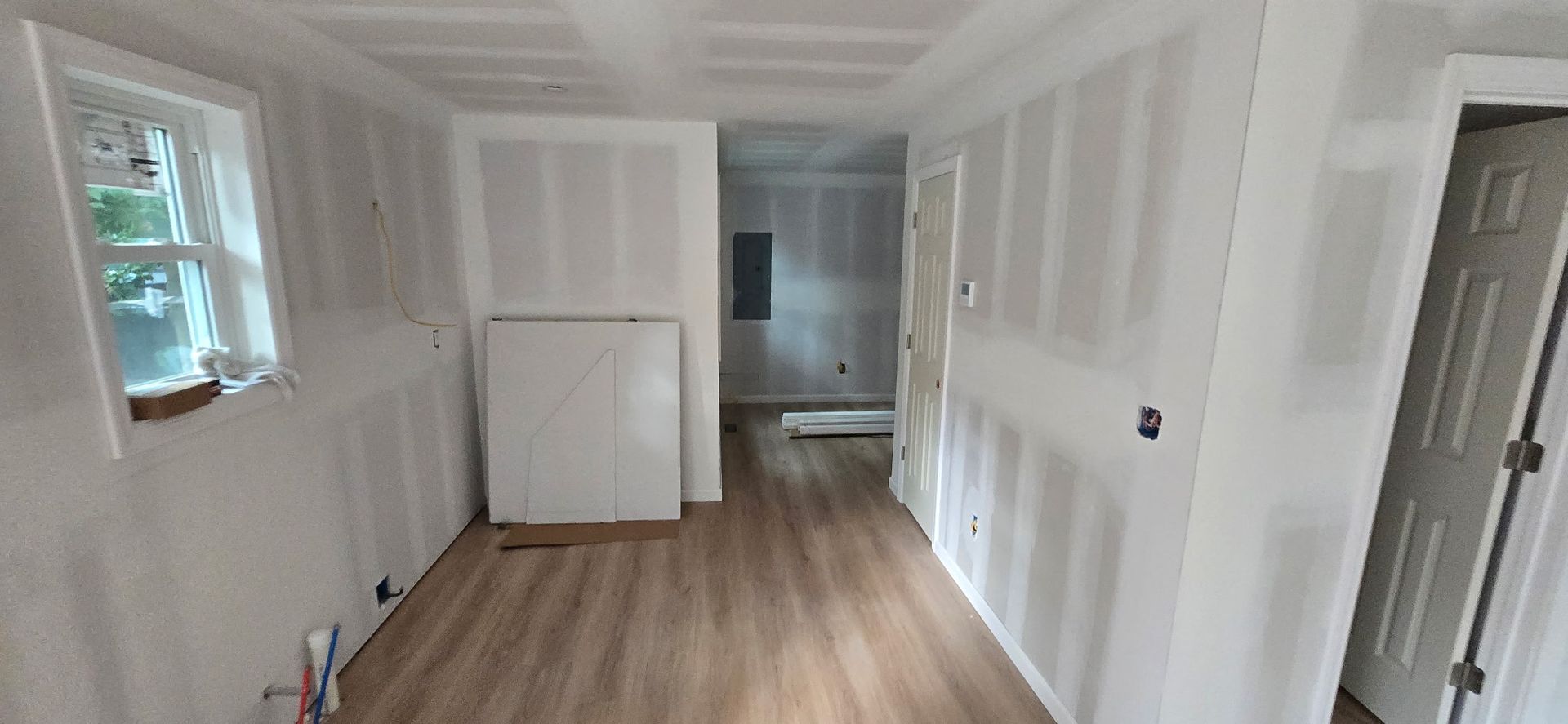 Interior view of a room under construction with white walls, wood flooring, and a cabinet. A window is on the left.