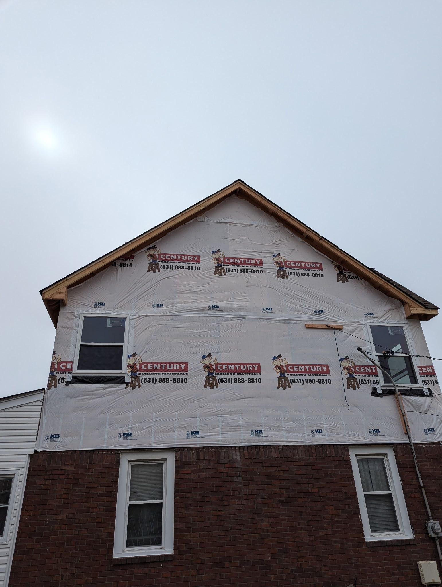 House exterior under construction, with sheathing, windows, and exposed roof framing against a cloudy sky.