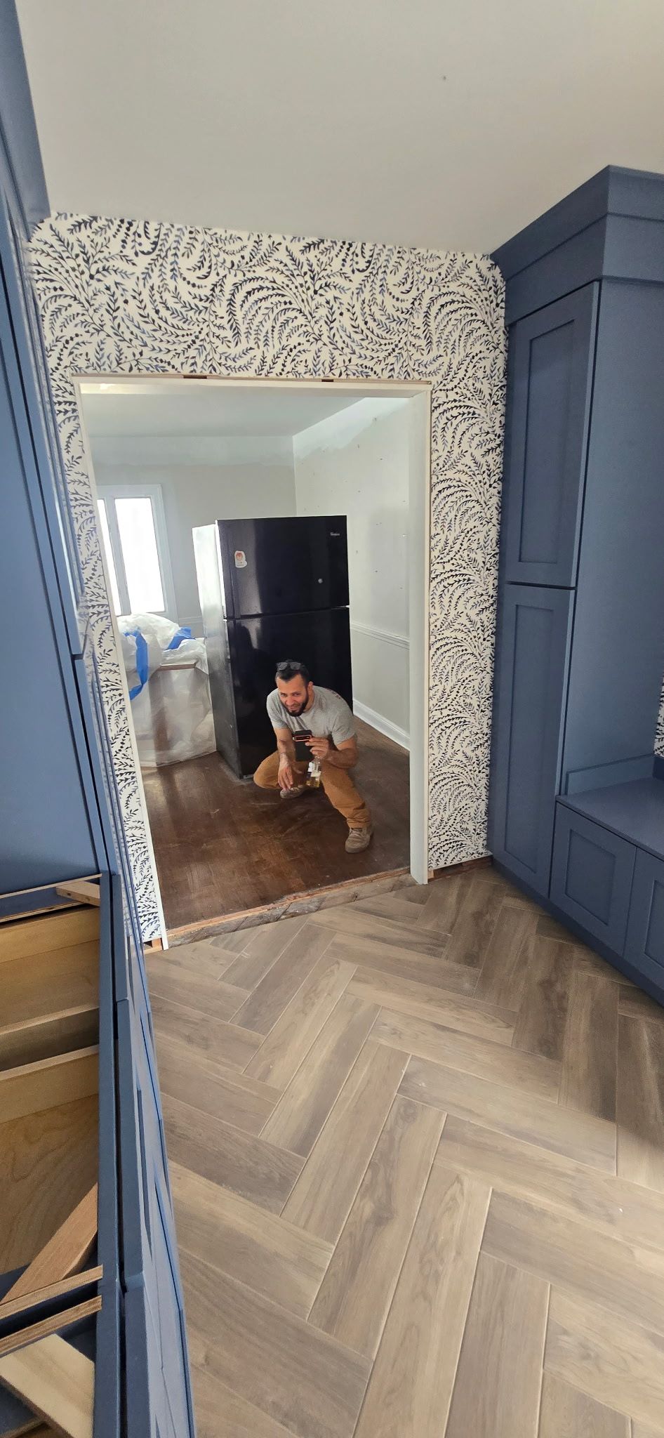 A person crouches in a doorway, looking toward the camera. Herringbone floor and speckled accent wall.