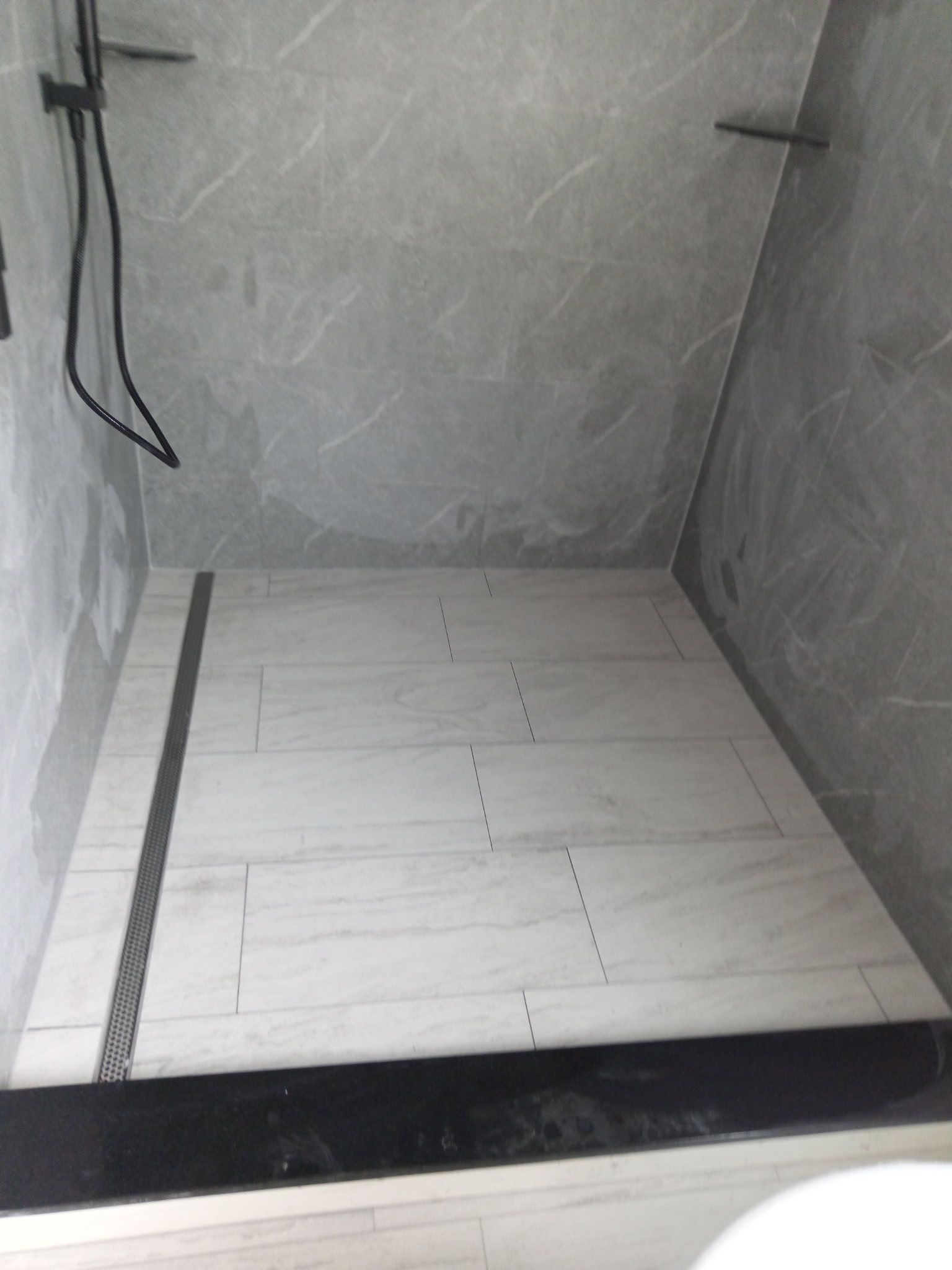 Empty shower with gray tiled walls and floor, linear drain, and black trim.