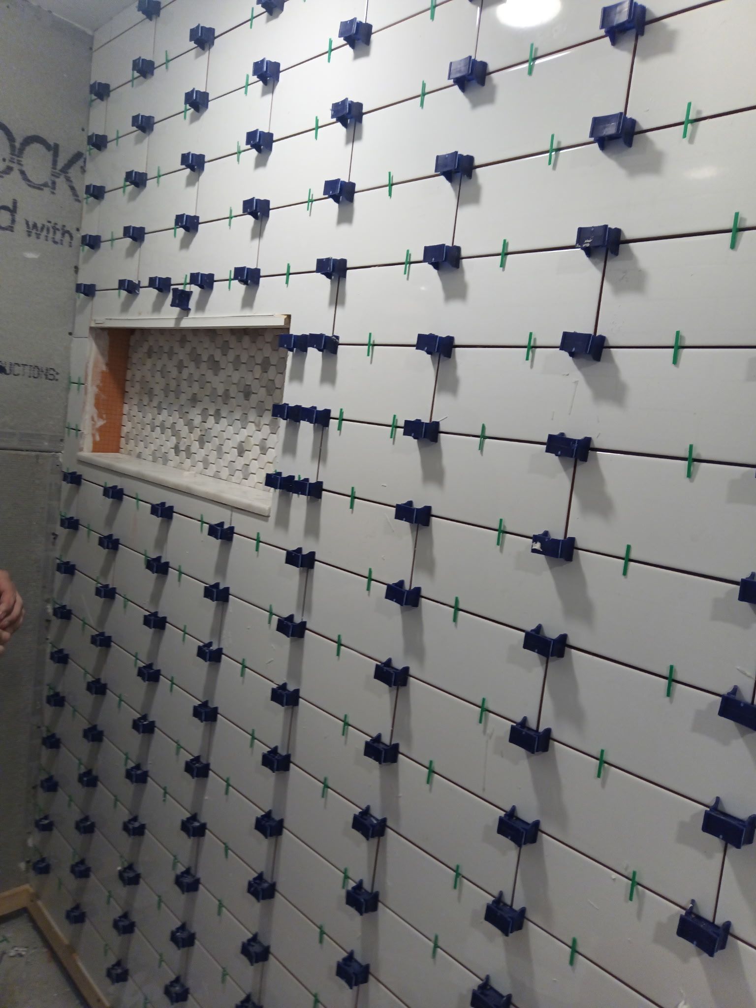 White tiled bathroom wall with a niche, using leveling clips for installation.