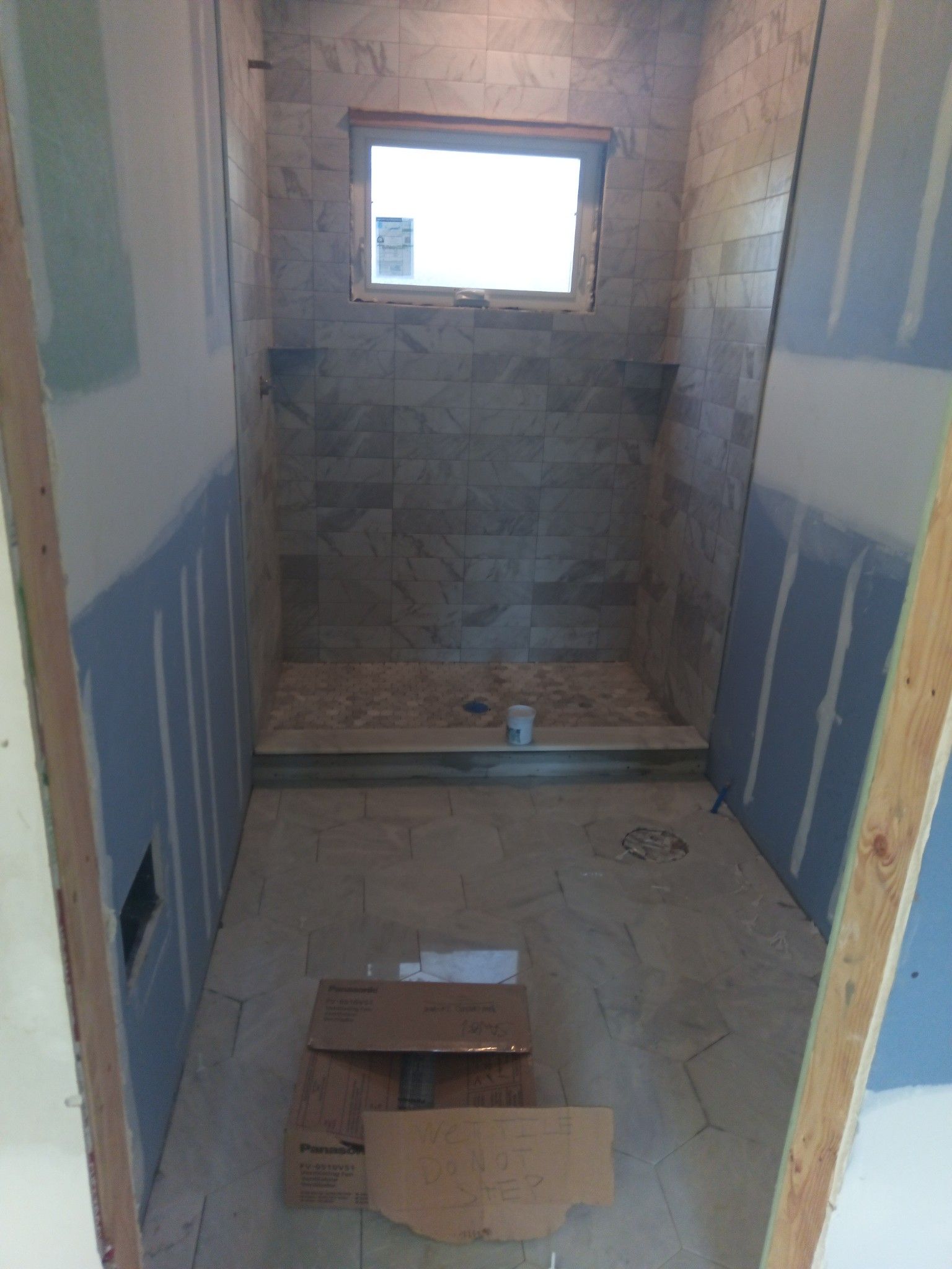 Bathroom under construction with tiled shower, small window, and unfinished walls.